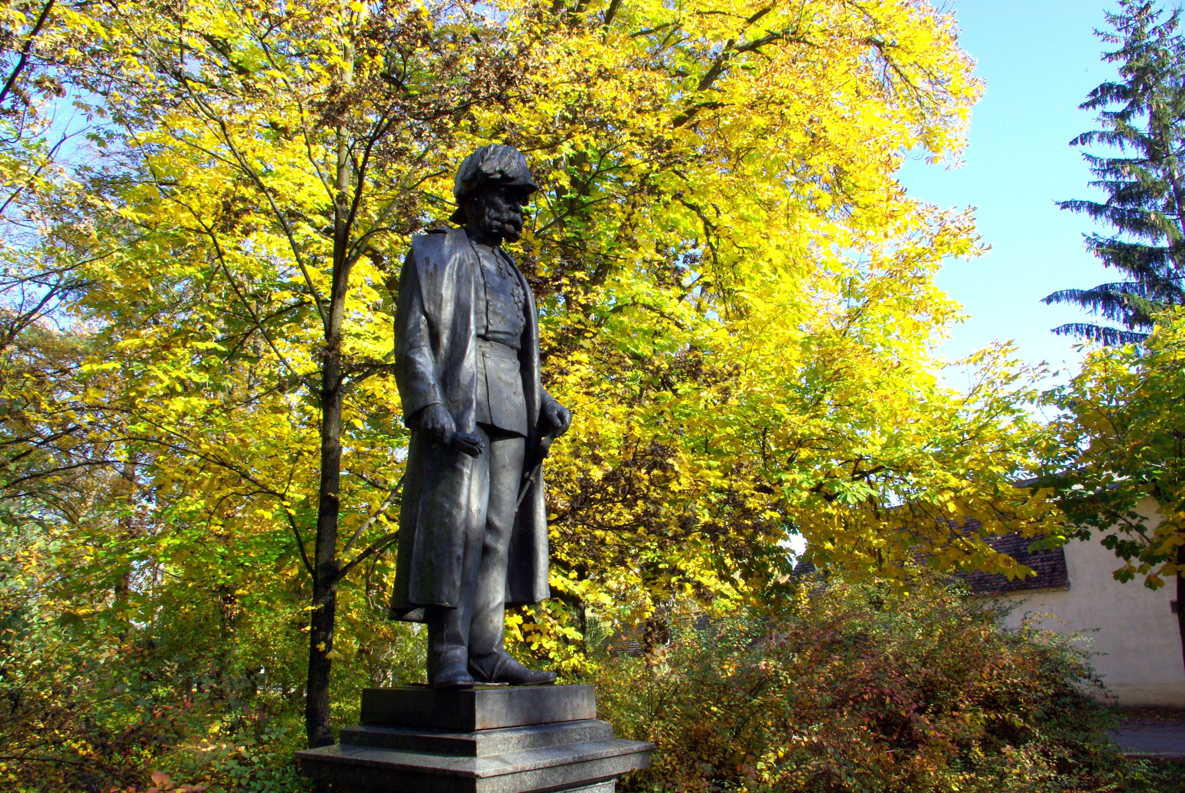 Statue of a man in an autumn park with yellow leaves in the background.