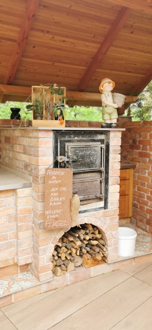 Brick oven with wood storage and decorations under a wooden roof.
