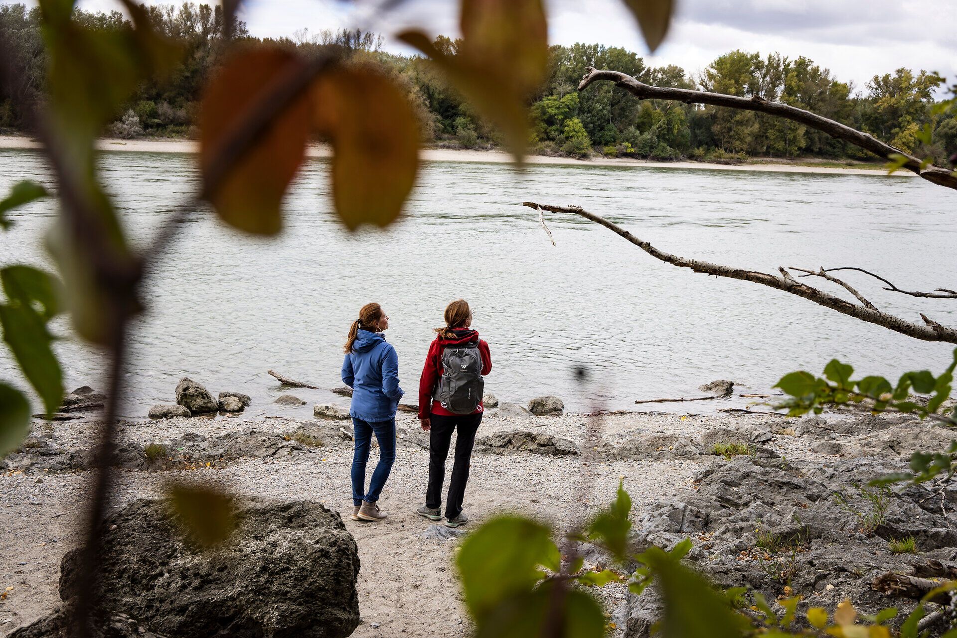 Two women stand on the banks of the Danube and look out over the water. 