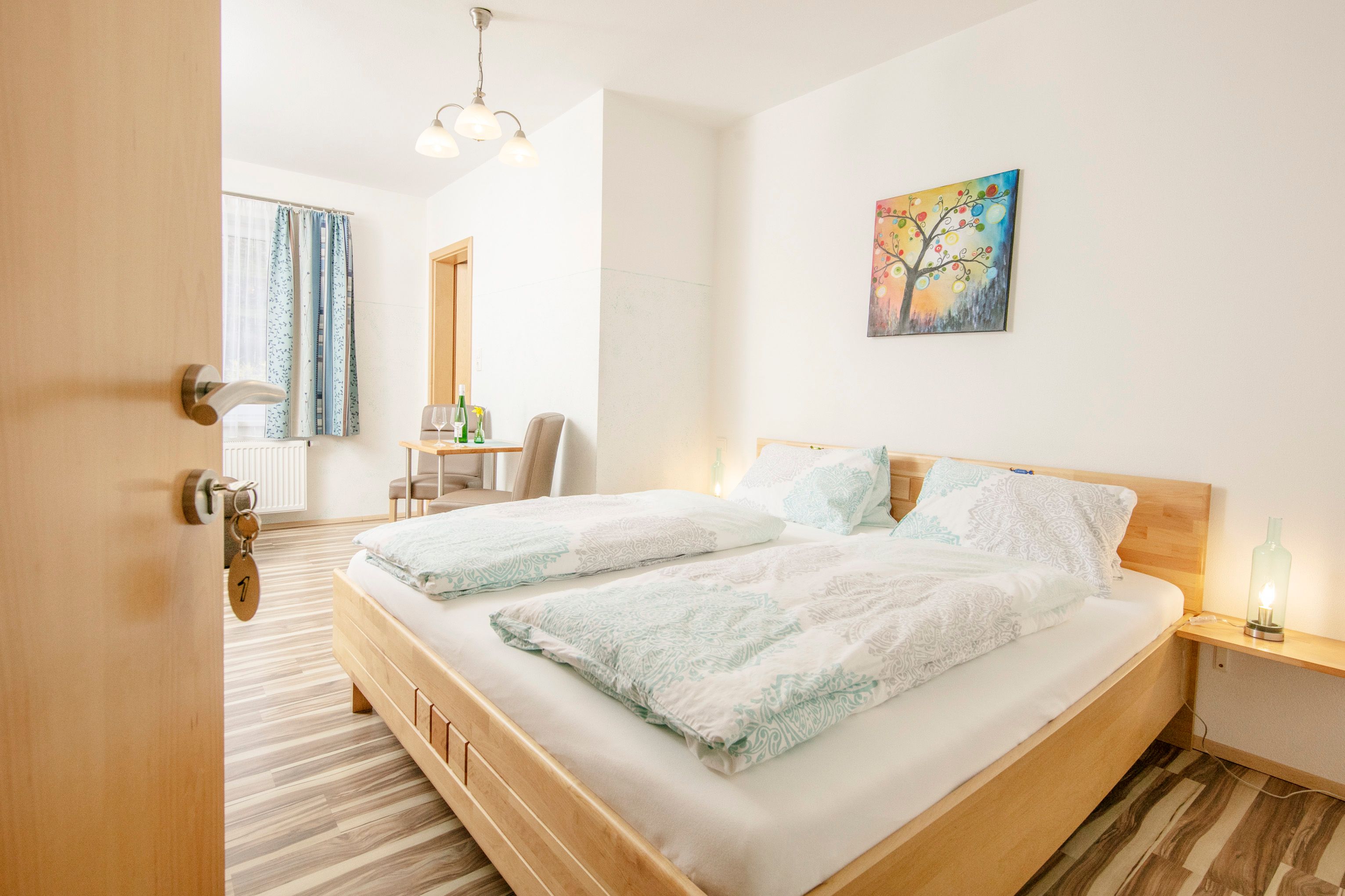 A bright guest room with a double bed, table, chairs and a colorful mural.