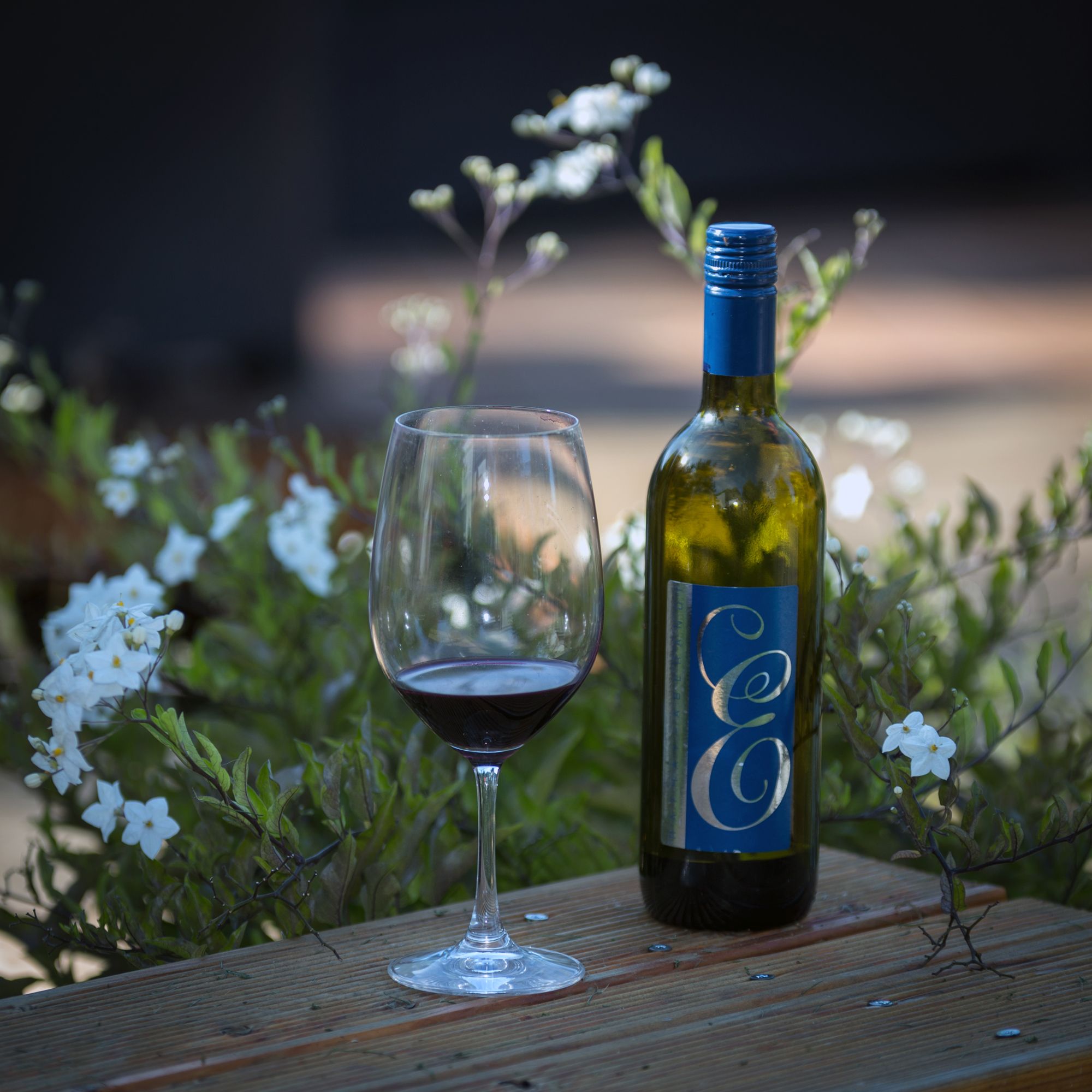 Wine bottle and glass on a wooden table with flowers in the background.