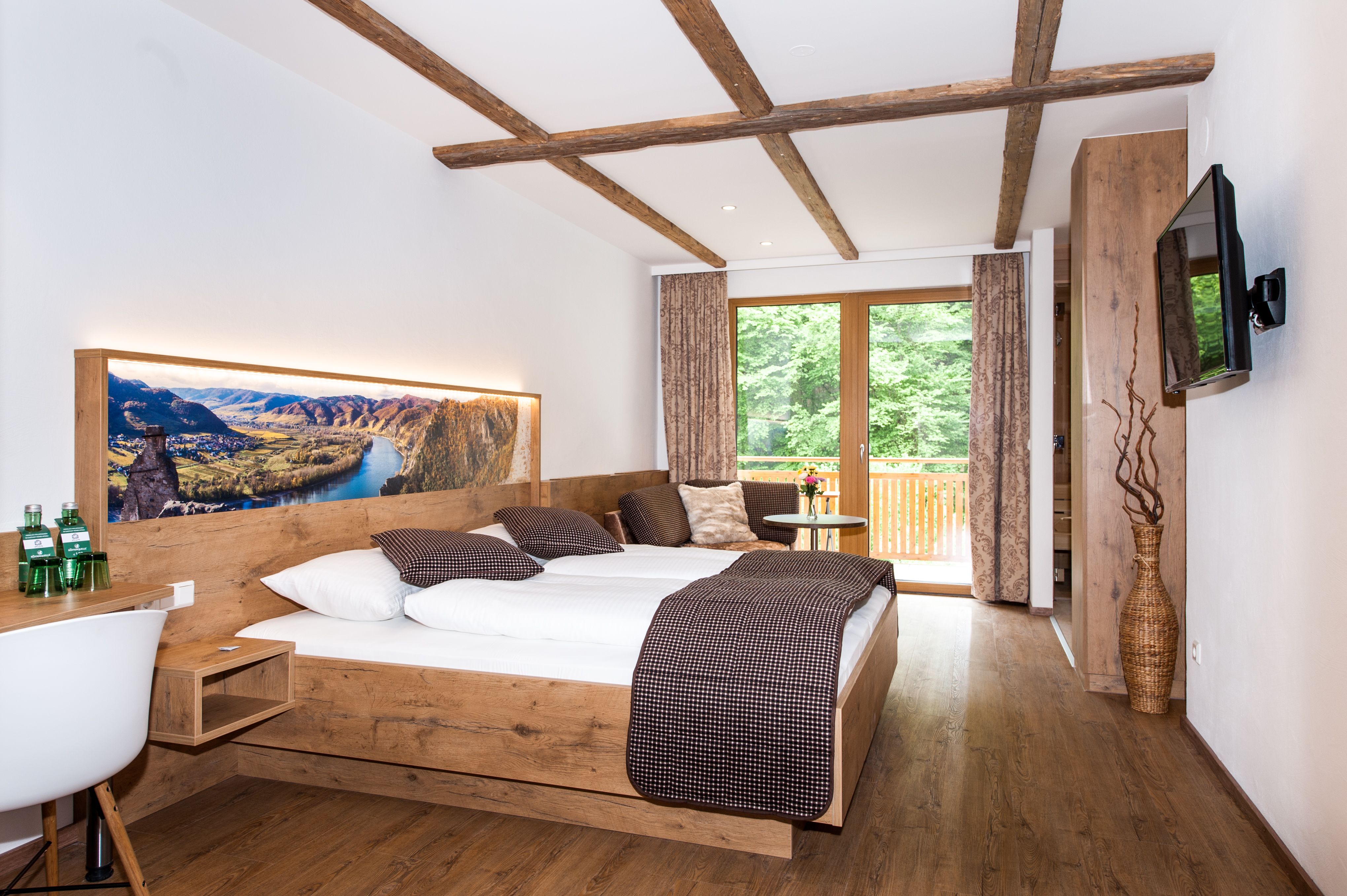 Modern hotel room with wooden furniture, large bed and balcony with a view of the countryside.