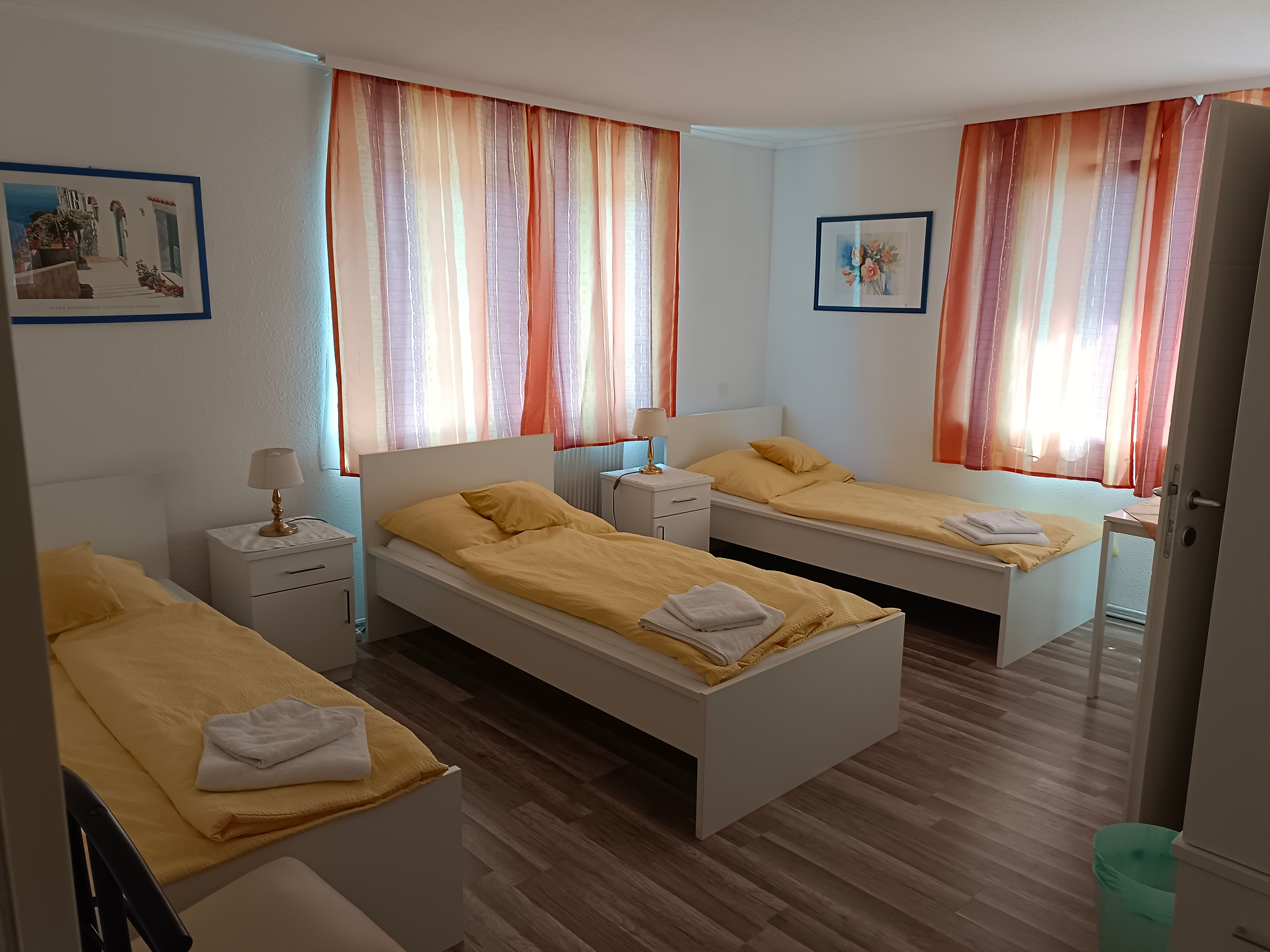 Three single beds in a bright room with yellow bed linen and colorful curtains.