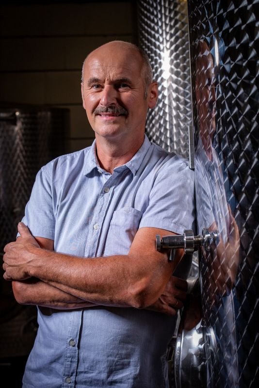 Man in blue shirt leaning against a metal tank in a brewery.