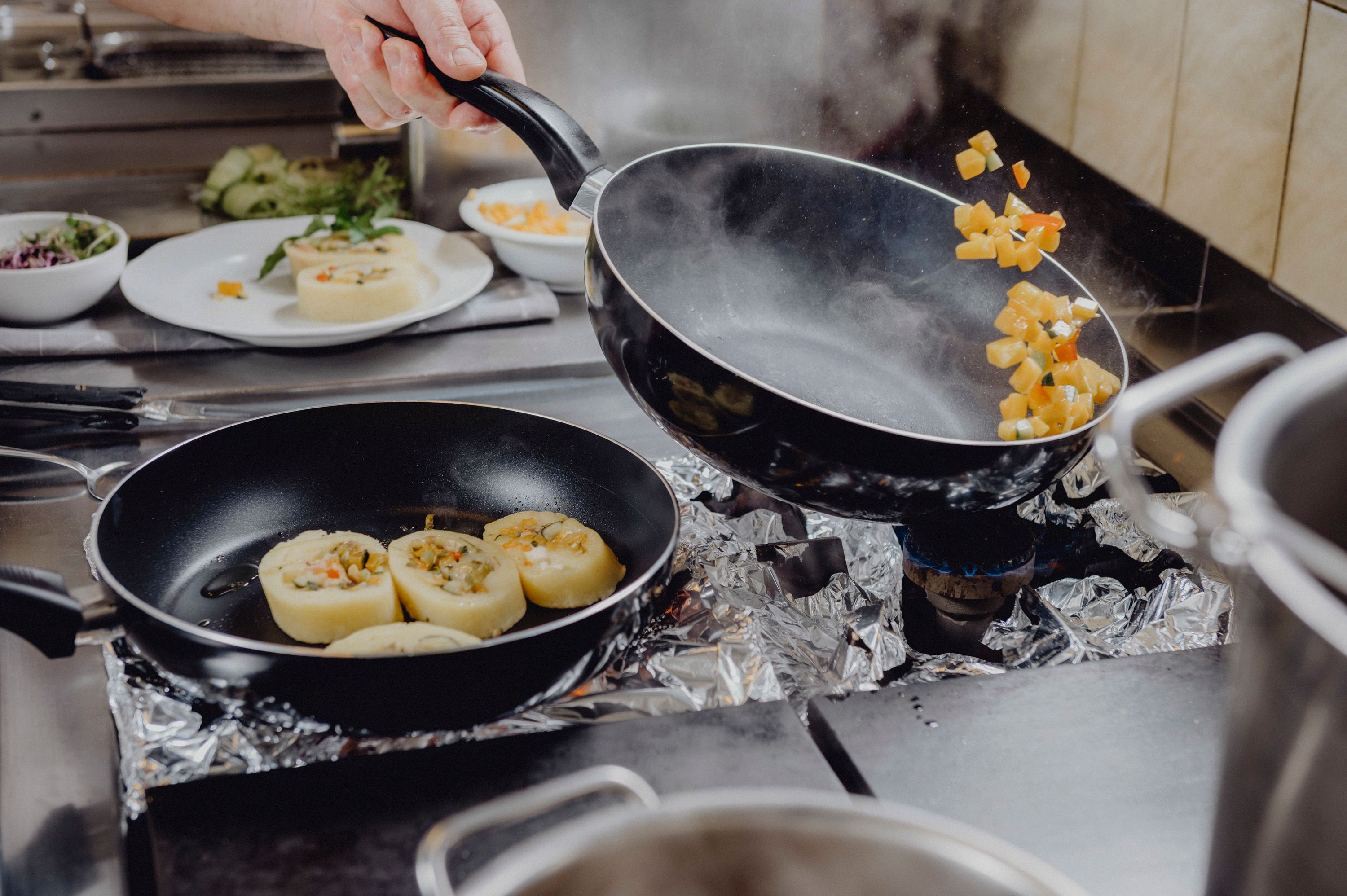 Cook tosses vegetables in a pan on a stove.
