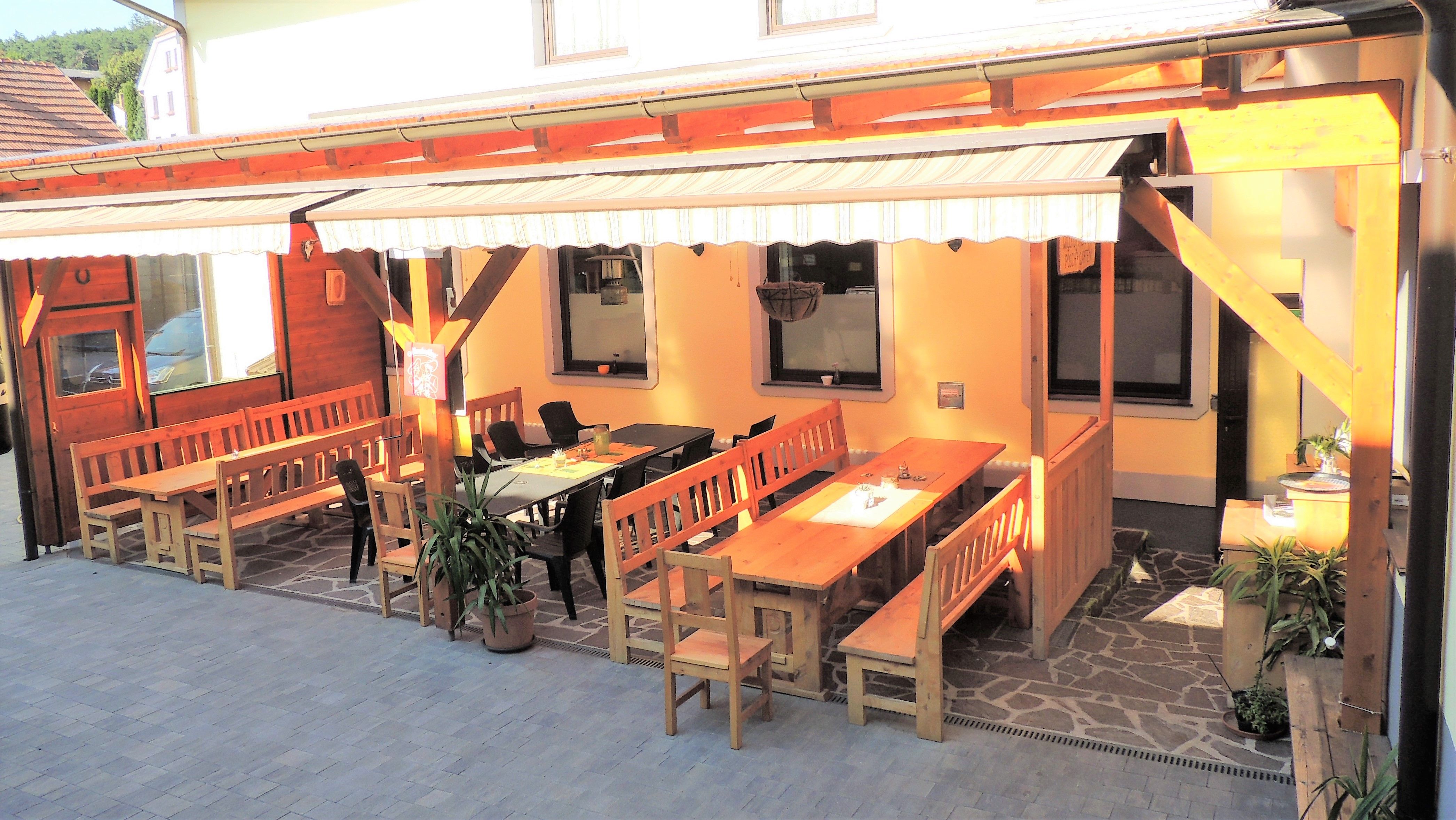 A cozy guest garden with wooden benches and tables under an awning.