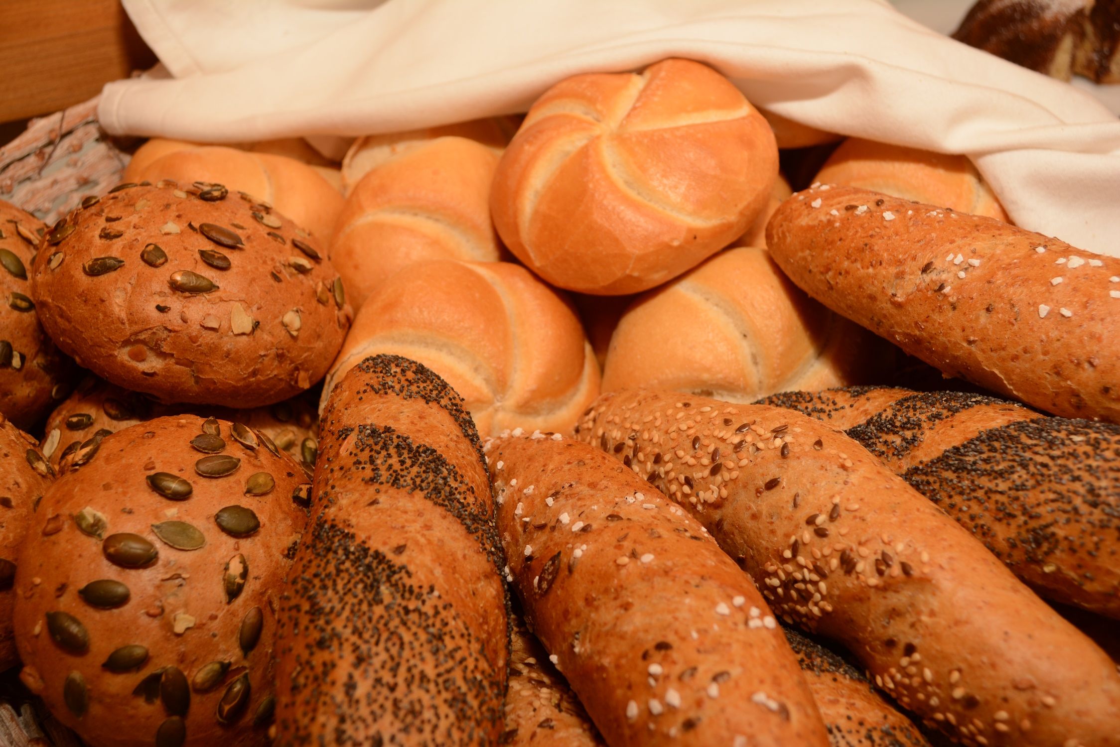 Various types of breakfast pastries, including rolls and baguettes with grains.