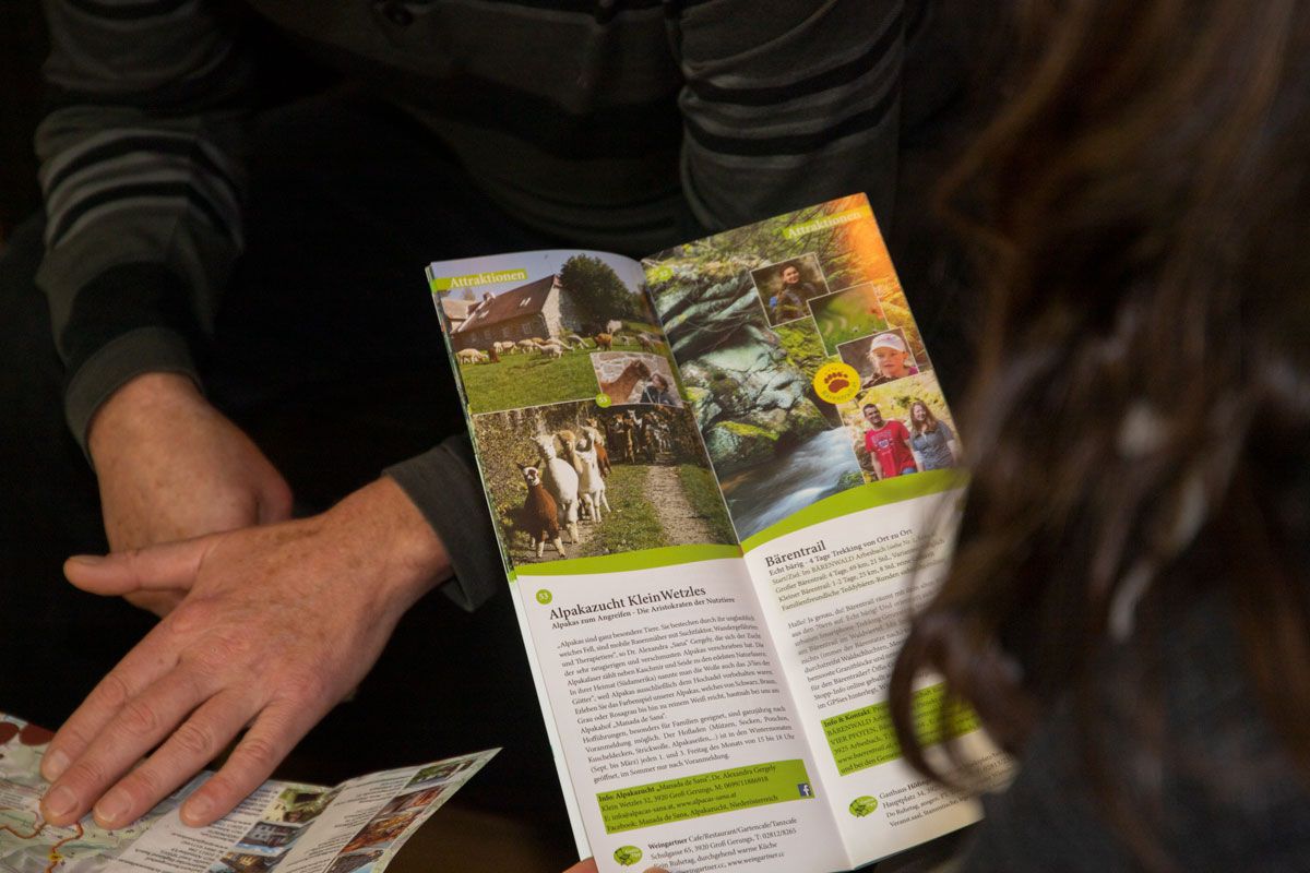 Two people leaf through a travel guide with pictures of alpacas and landscapes.