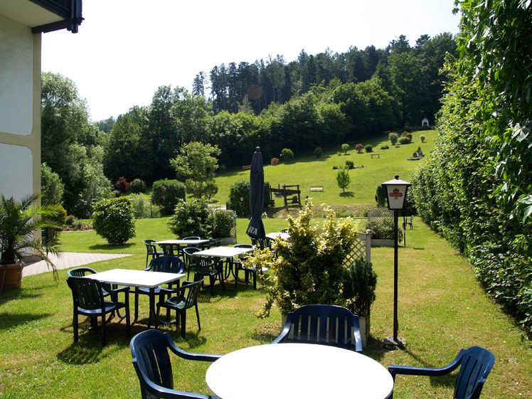 Garden with tables and chairs, surrounded by trees and meadows.