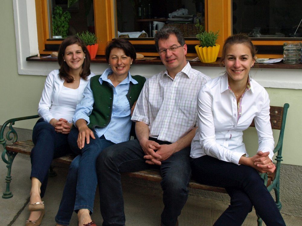 Four people are sitting on a bench in front of a window with plants.