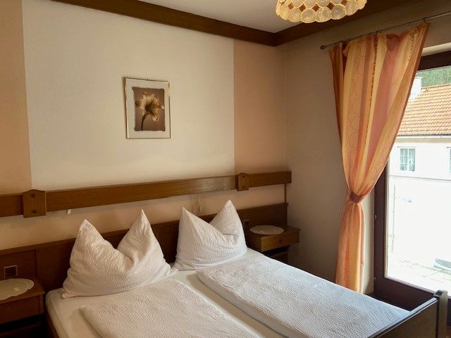 A cozy double room with two beds, a window with a curtain and a picture on the wall.