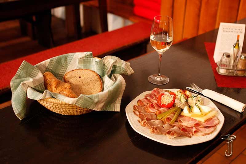 A table laid with a platter of cold meats, a basket of bread and a glass of white wine.