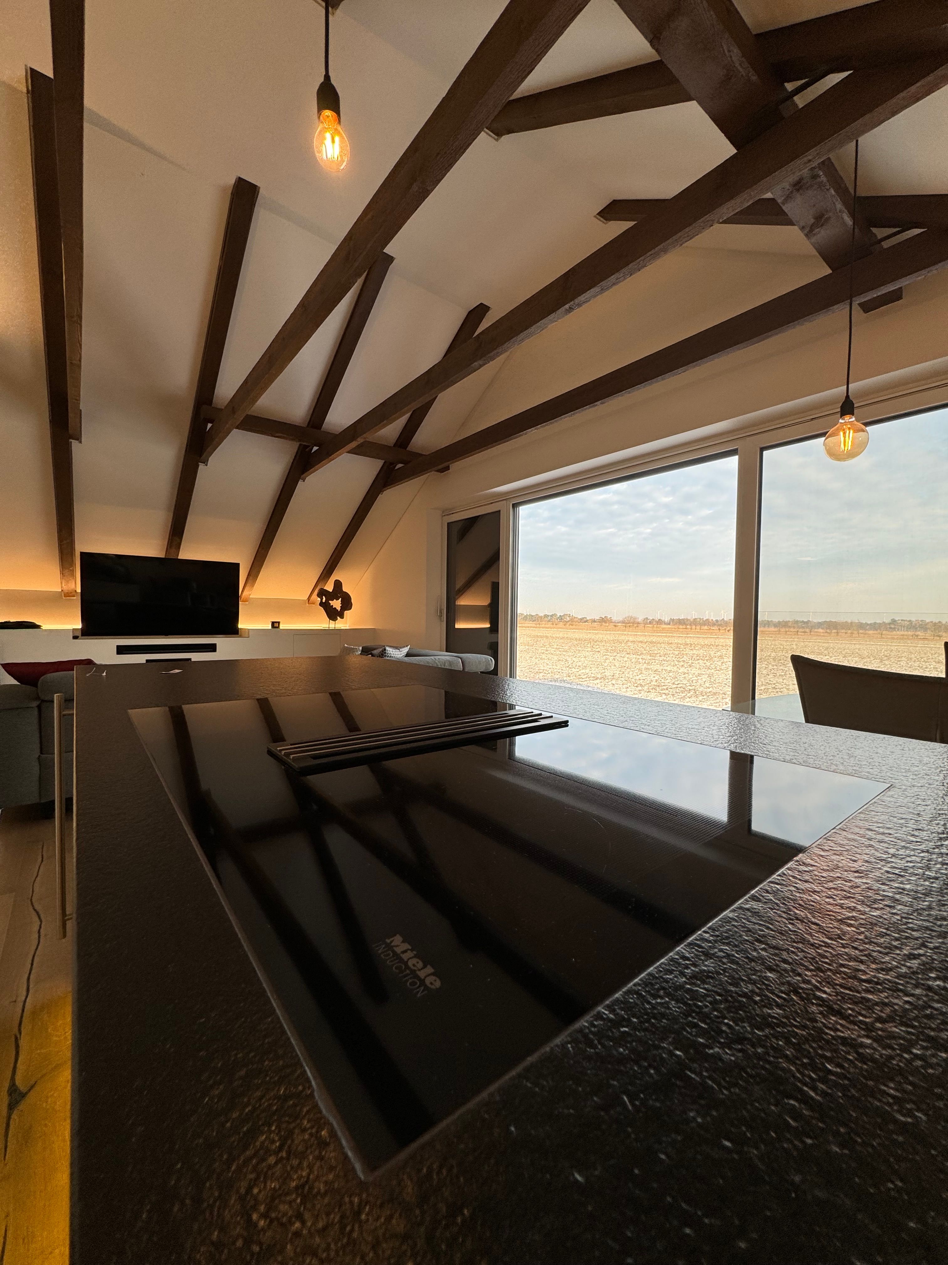 Modern living and dining area with wooden beams, cooking island and large window with a view.