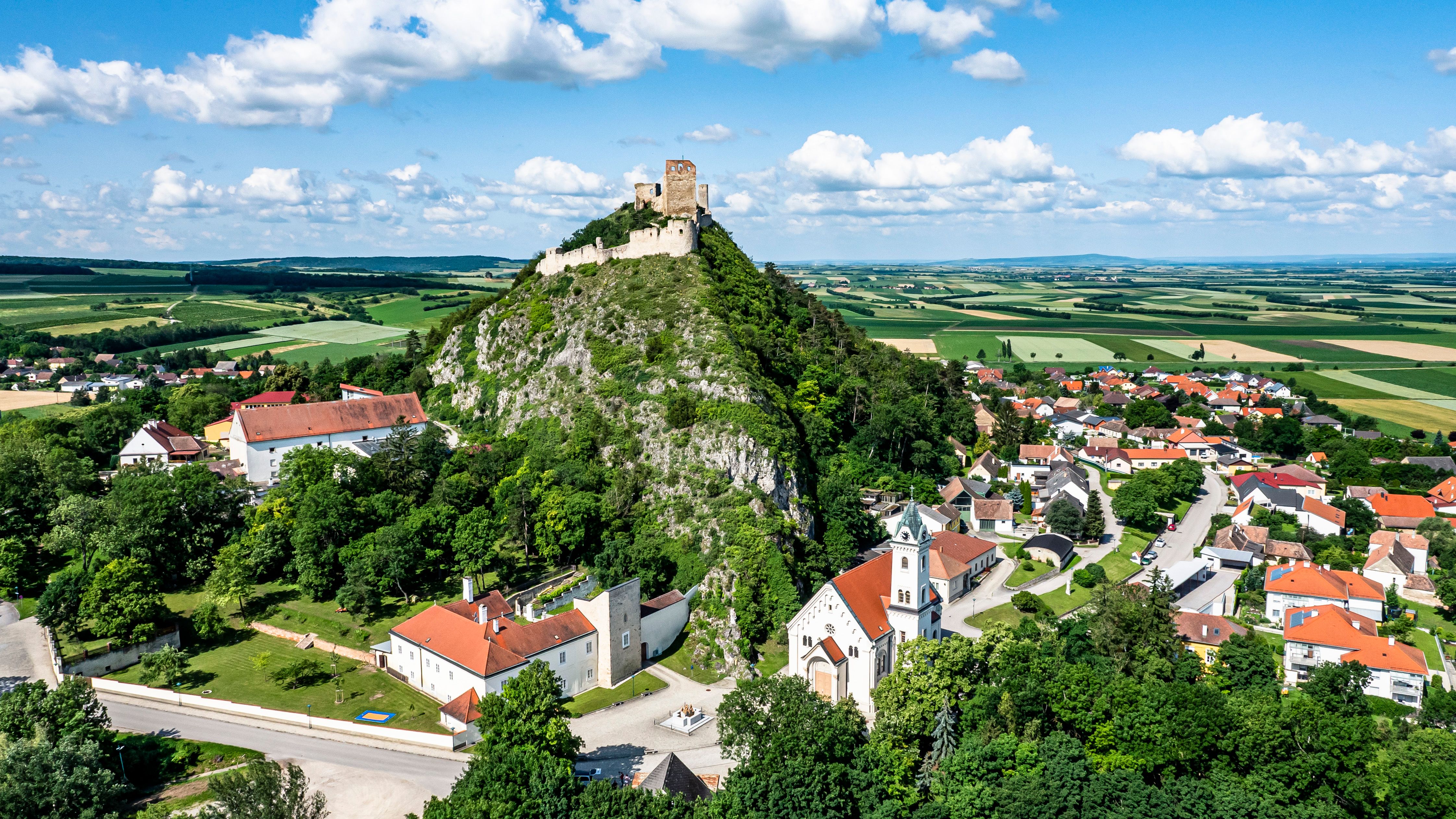 Aerial view of a castle on a hill with surrounding village and fields.