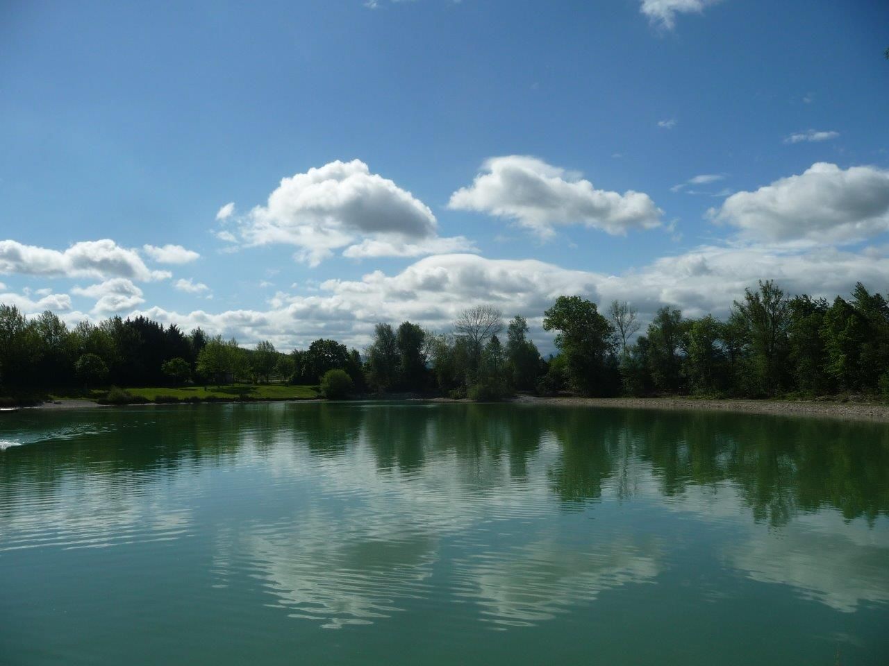 A calm lake with trees and clouds reflected in the water.