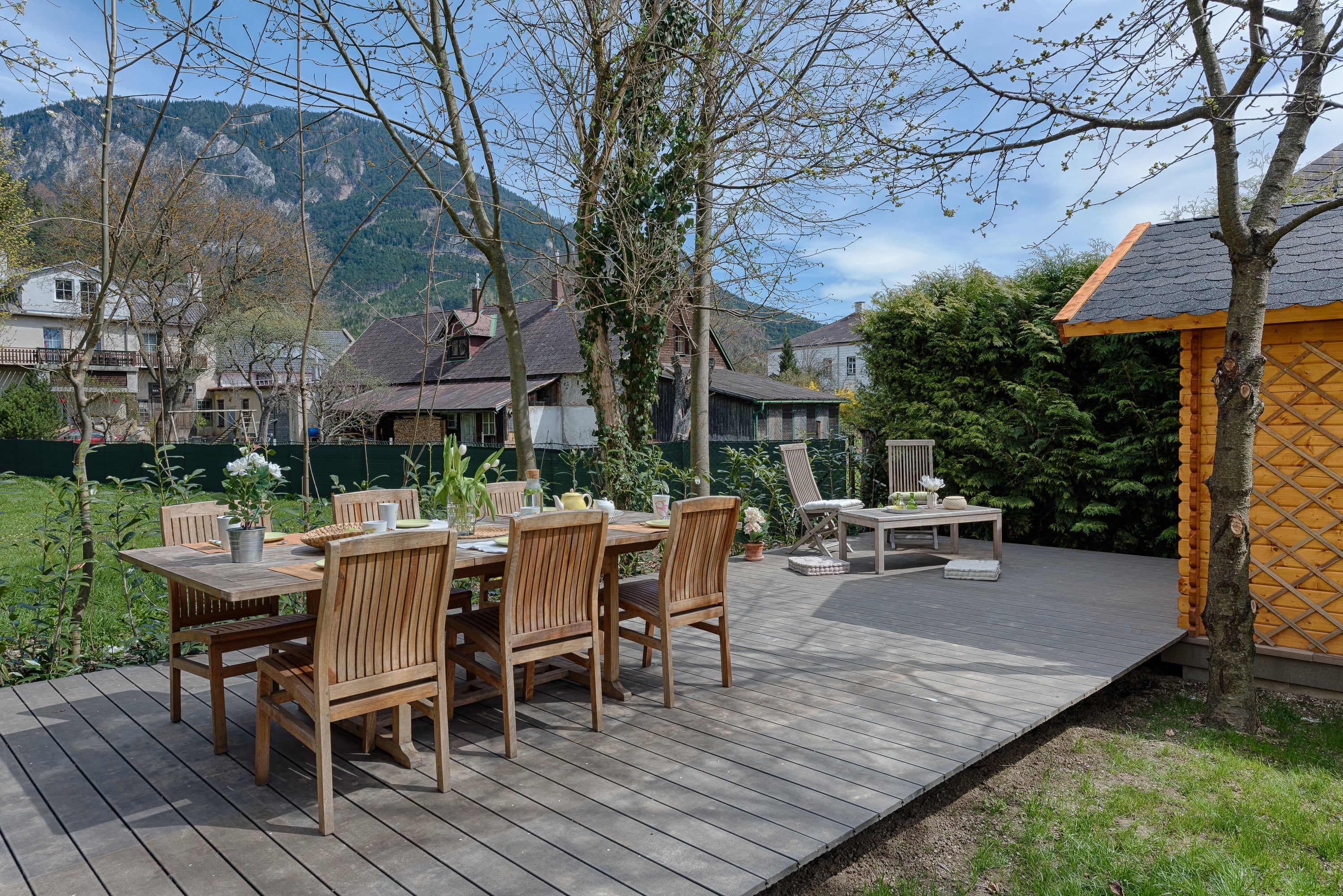 Wooden terrace with table and chairs, surrounded by trees and mountains in the background.