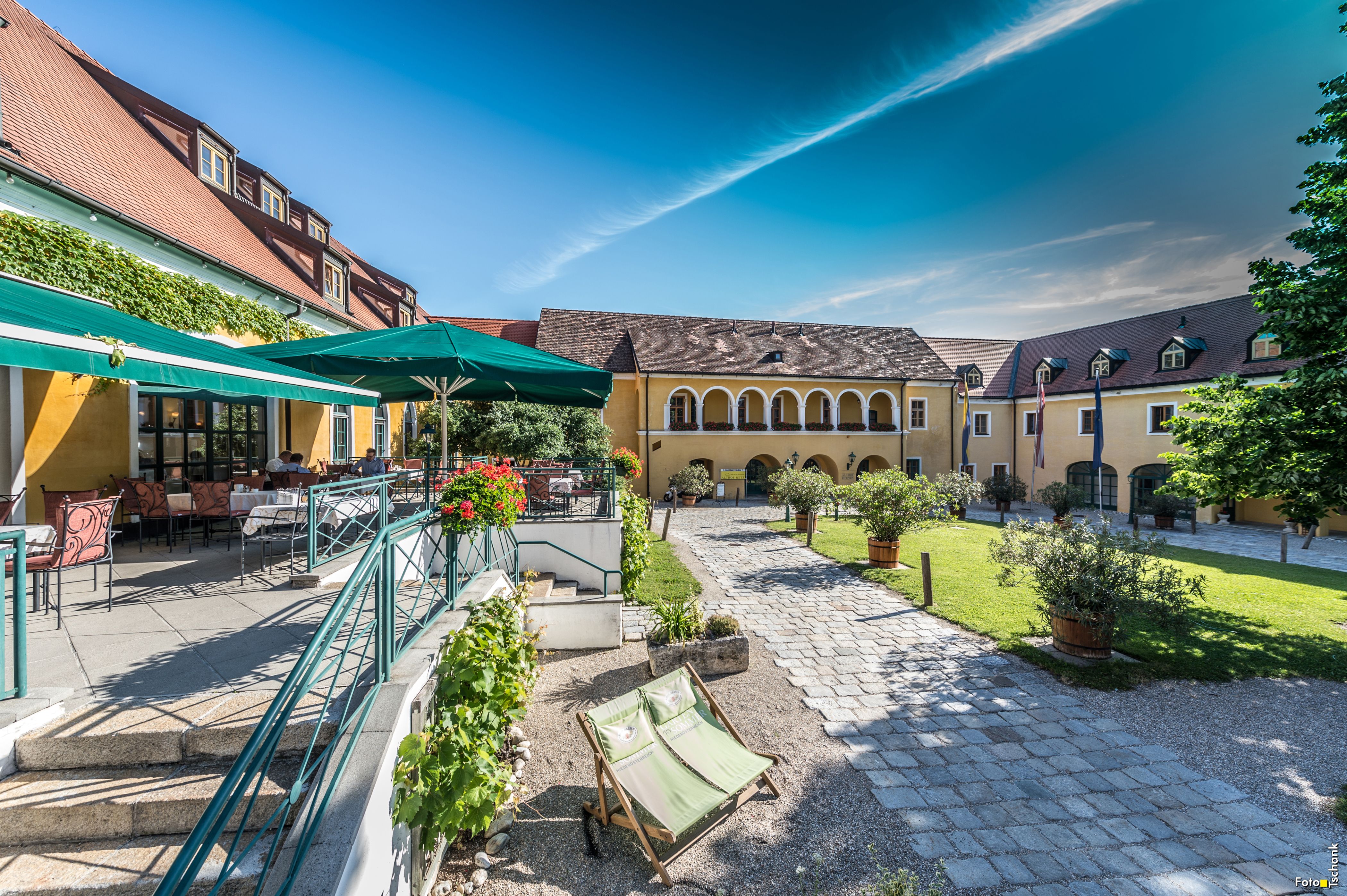 A sunny inner courtyard with yellow buildings, terrace area and sun loungers.