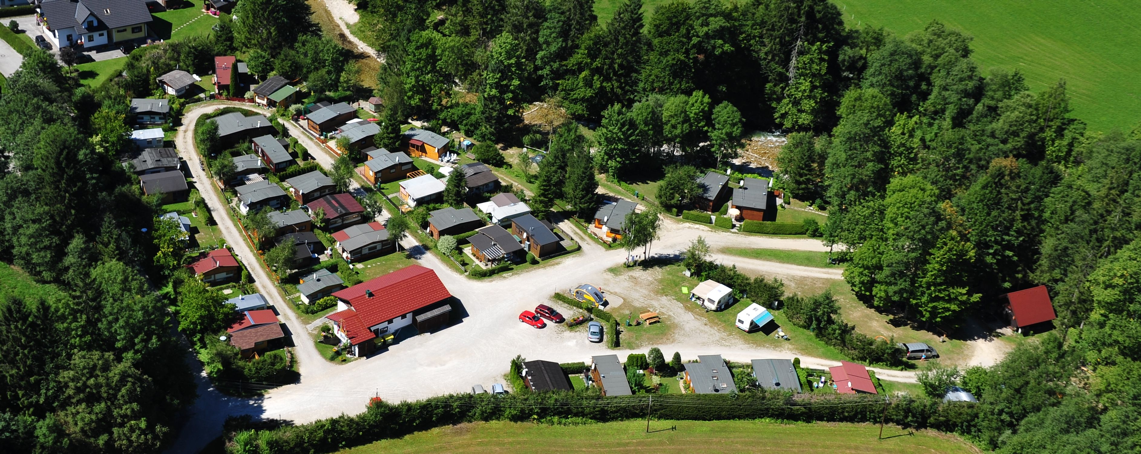 Aerial view of a campsite with caravans and small houses, surrounded by trees and meadows.