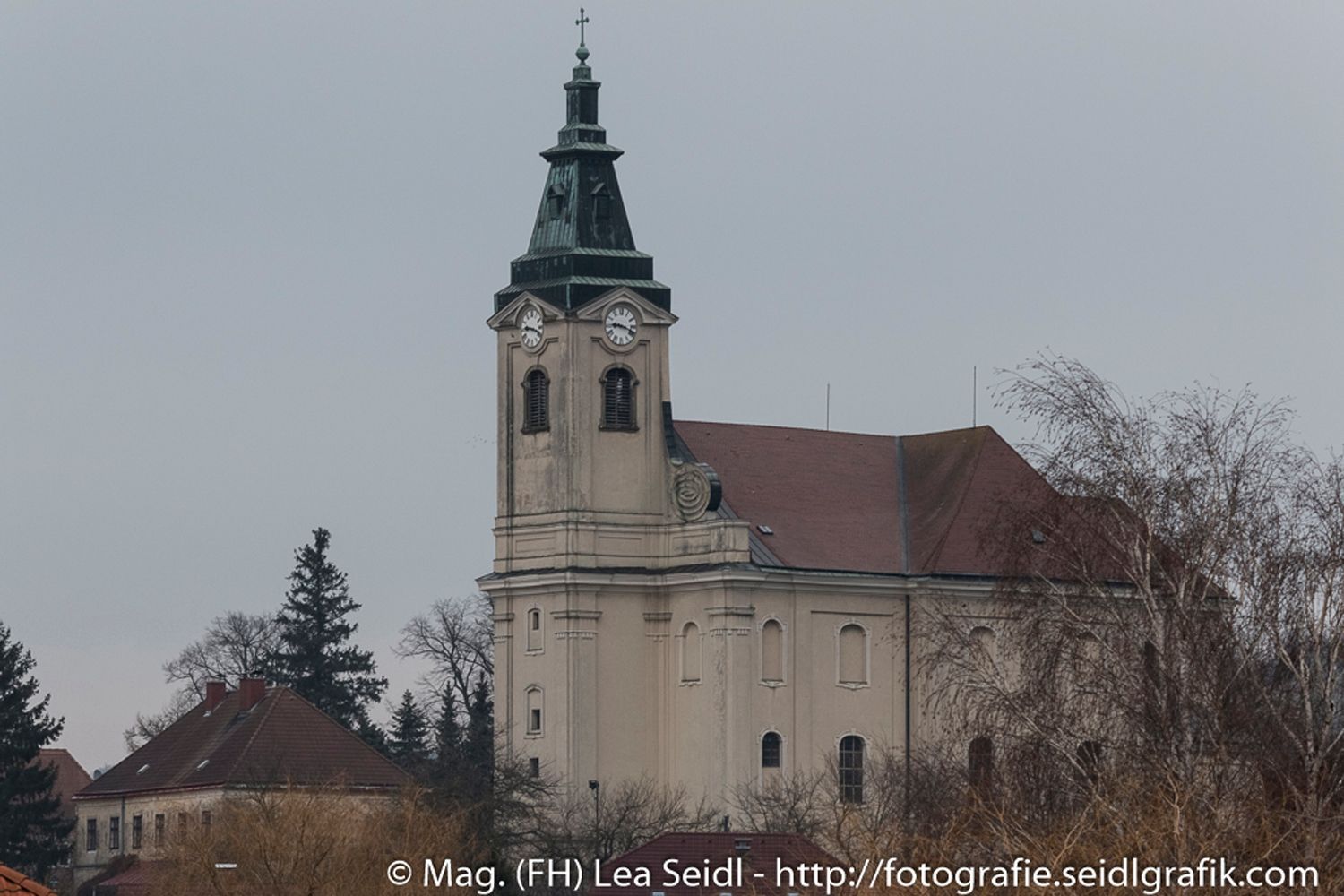 Church in Niederhollabrunn with tower and clock, surrounded by trees.