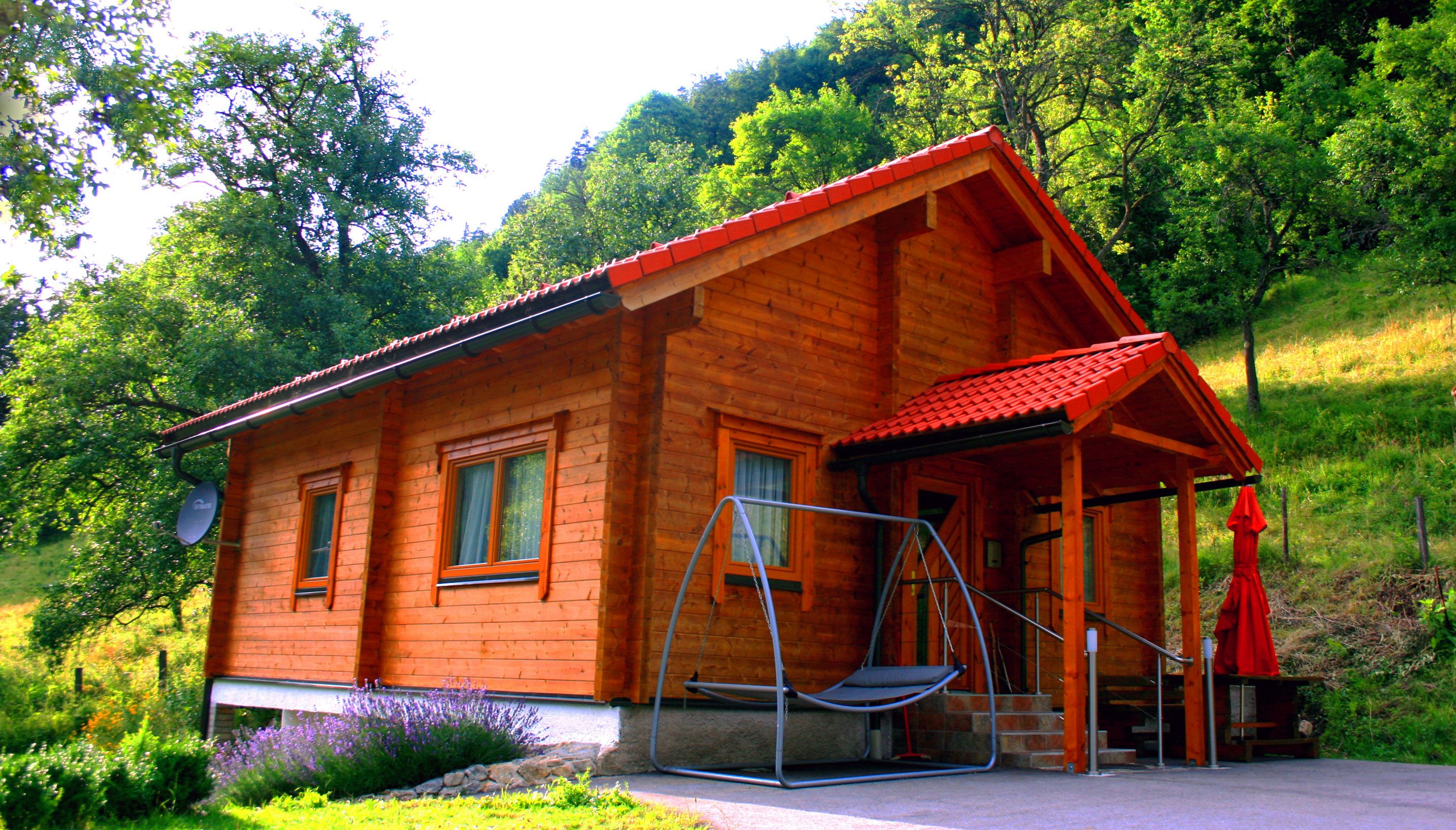 A wooden holiday home with a red roof in a green, wooded setting.