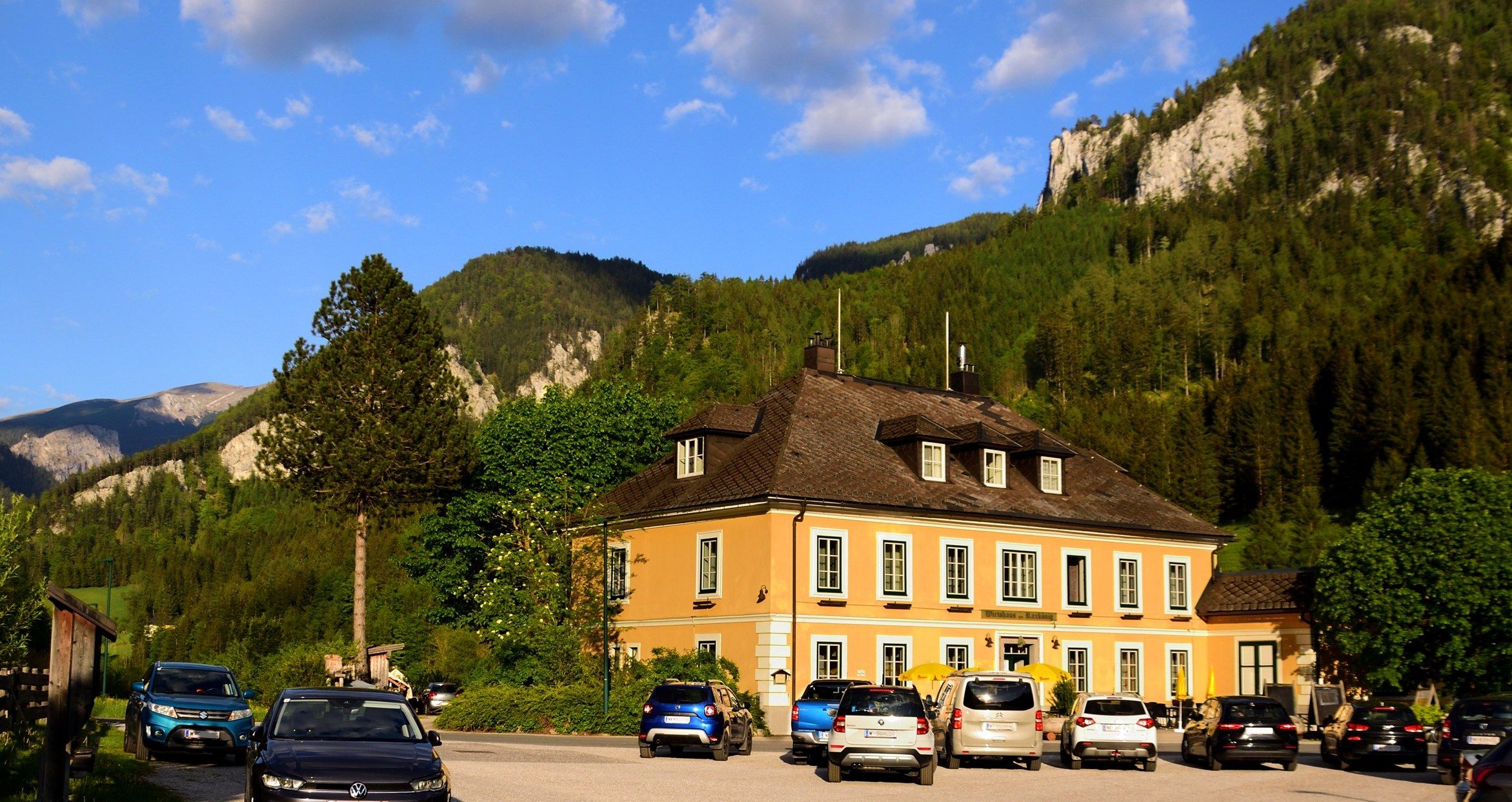 A yellow building against a mountain backdrop with parked cars in front of it.