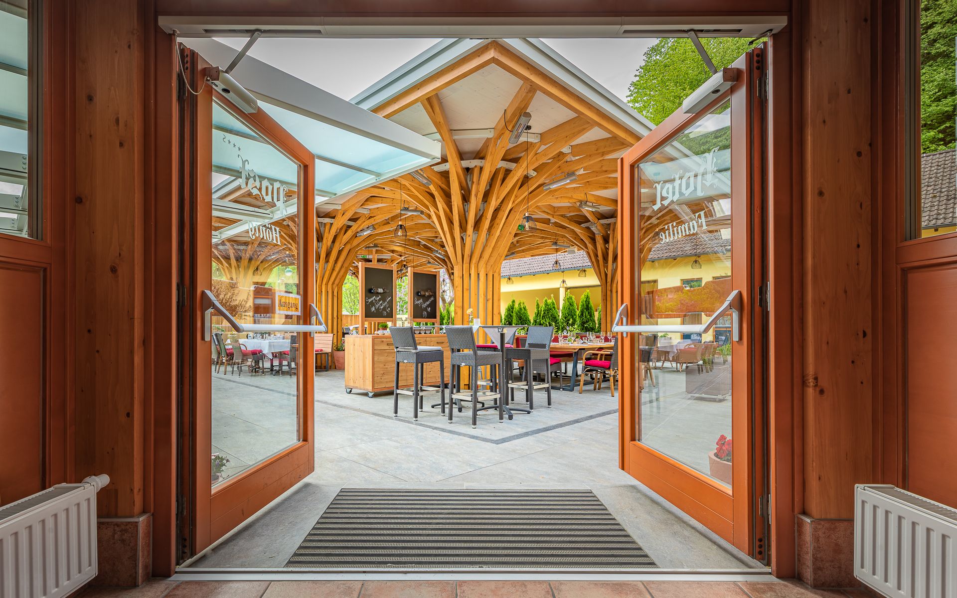 Open glass doors lead to a terrace with a wooden roof and seating.