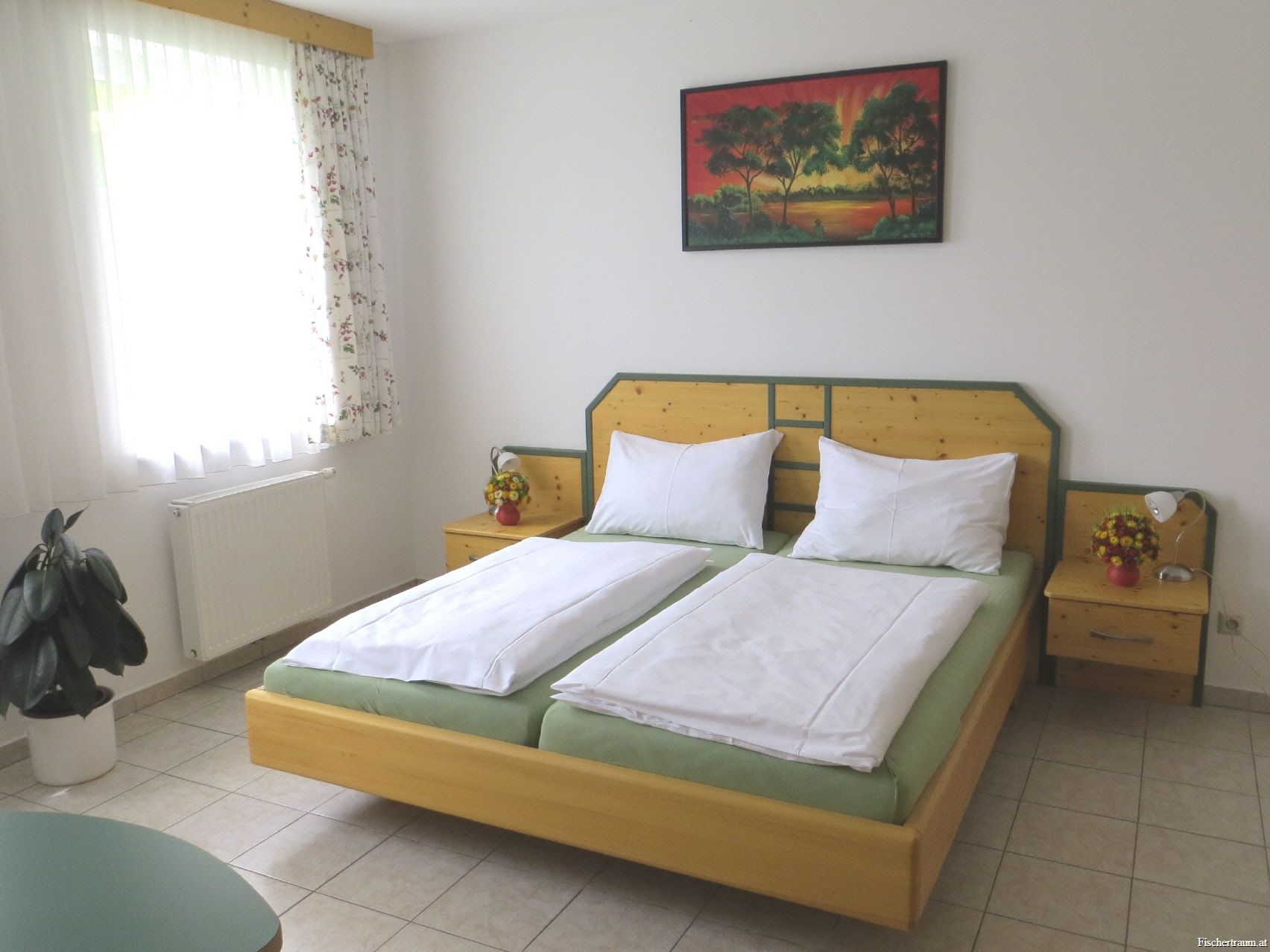 A guest room with a double bed, bedside tables, a picture on the wall and a window with curtains.