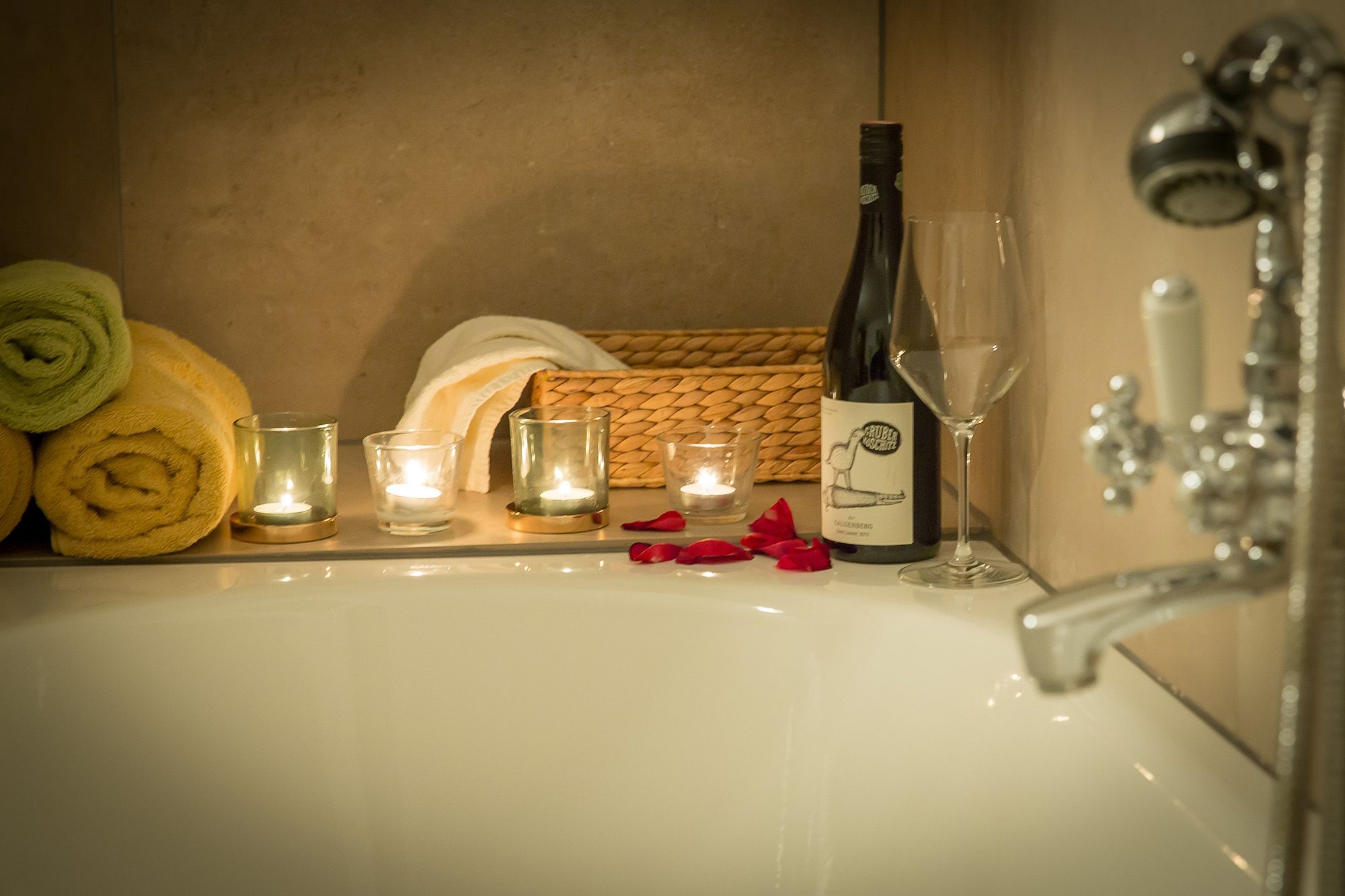 Romantic bathroom with candles, wine bottle and rose petals on the edge of the bathtub.