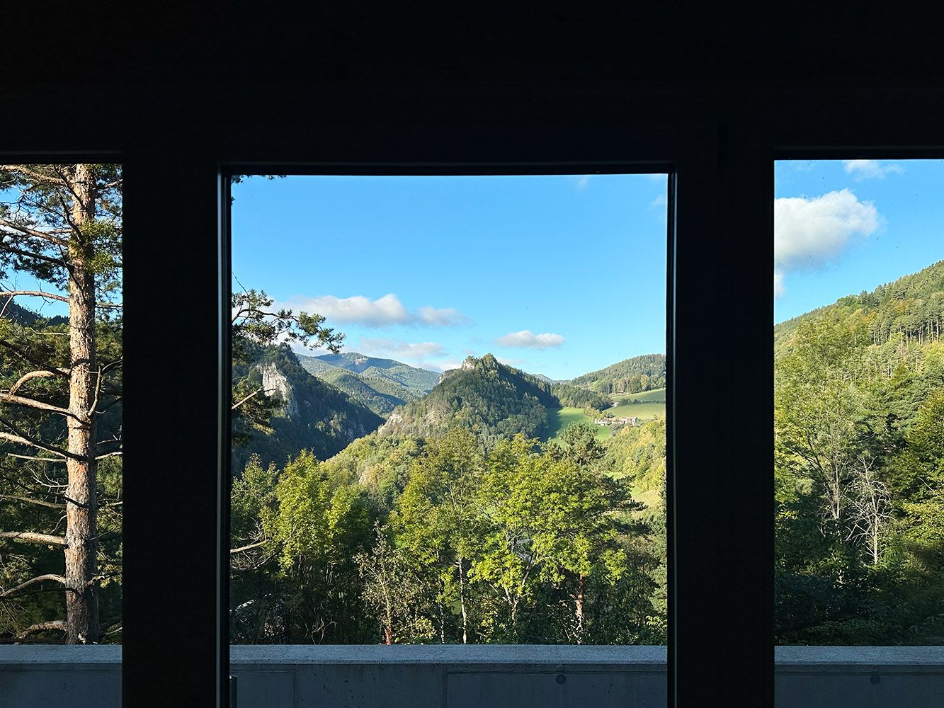 View from a window onto a green mountain landscape with a blue sky.
