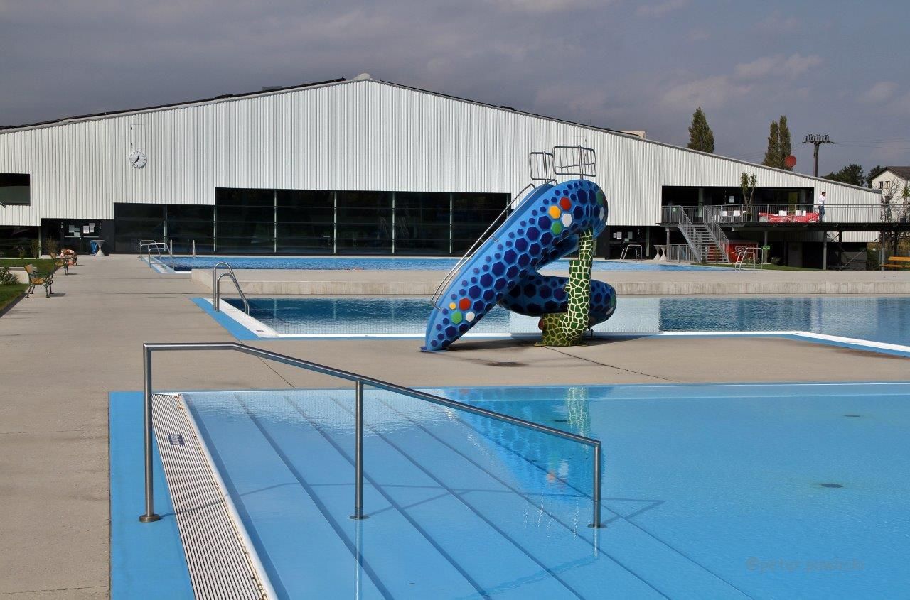 An empty outdoor pool with a colorful slide and a large building in the background.