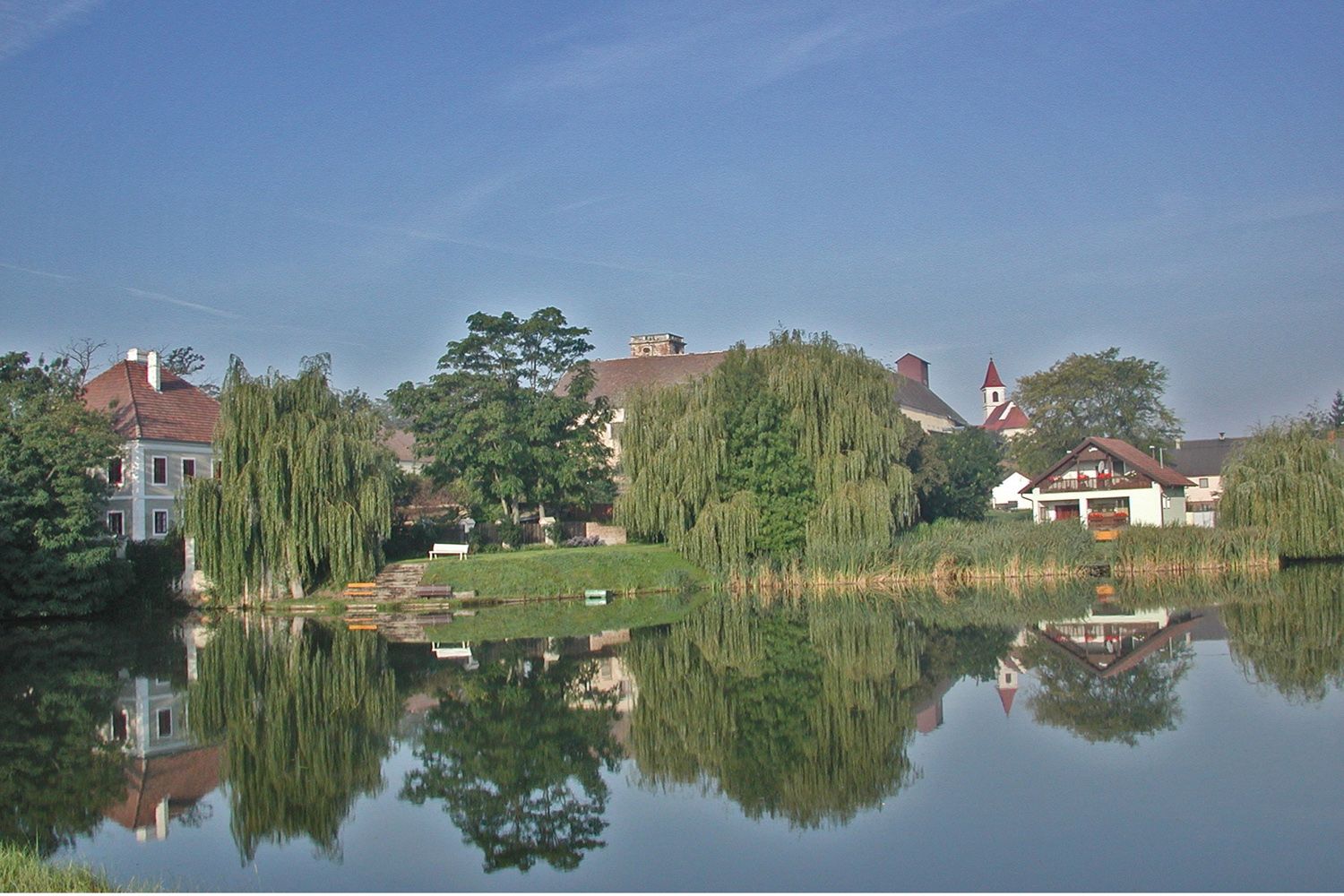 A tranquil pond with a reflection of trees and buildings in Niederabsdorf.