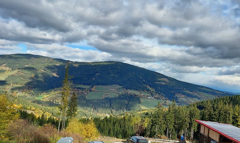 Panoramic view of a hilly landscape with forests and fields under a cloudy sky.