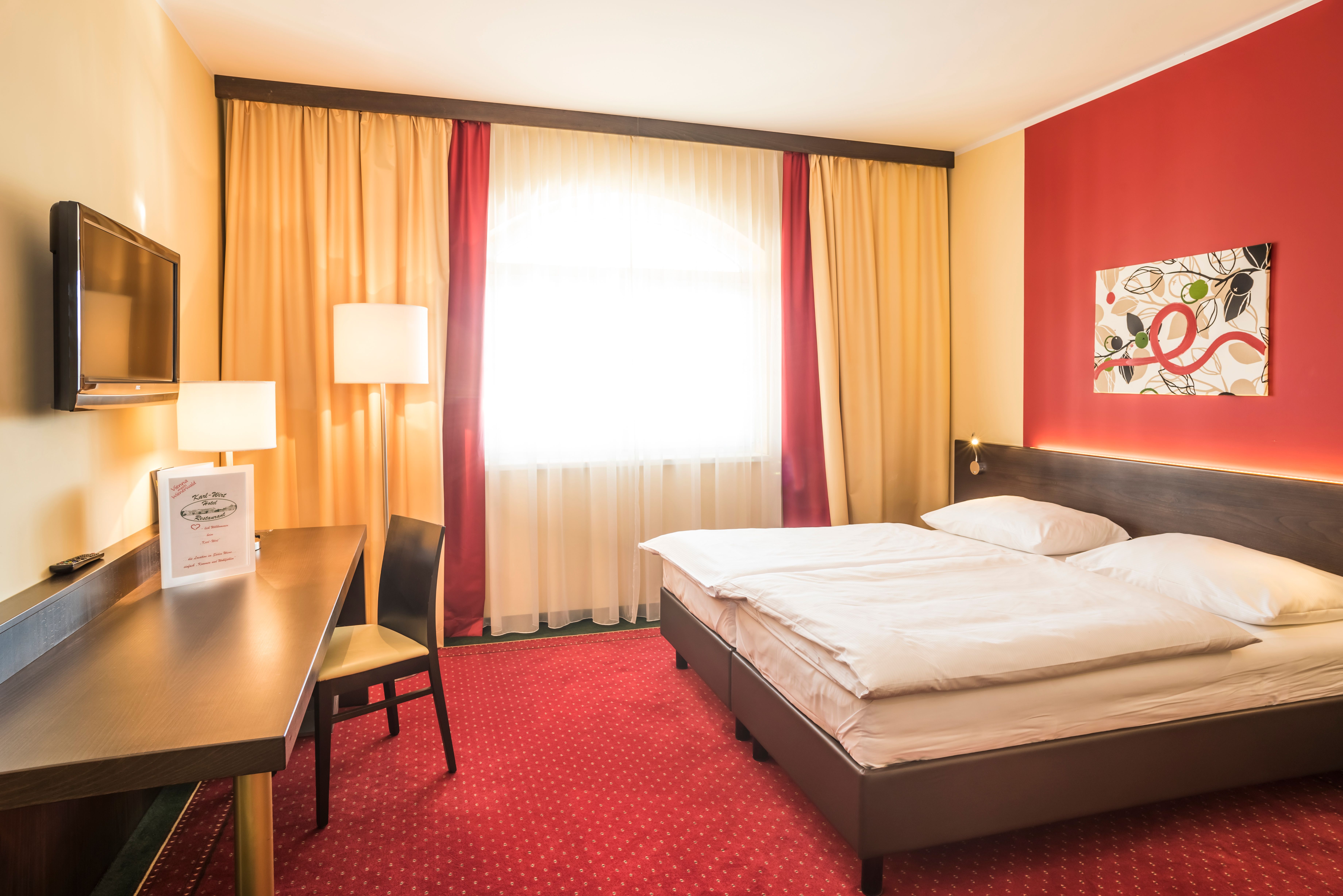 A cozy hotel room with a double bed, red carpet, desk, TV and modern art on the wall.