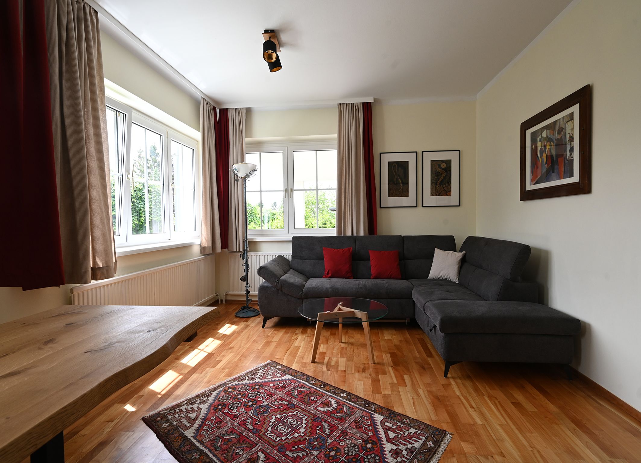 Modern living room with gray sofa, wooden table, carpet and large windows.