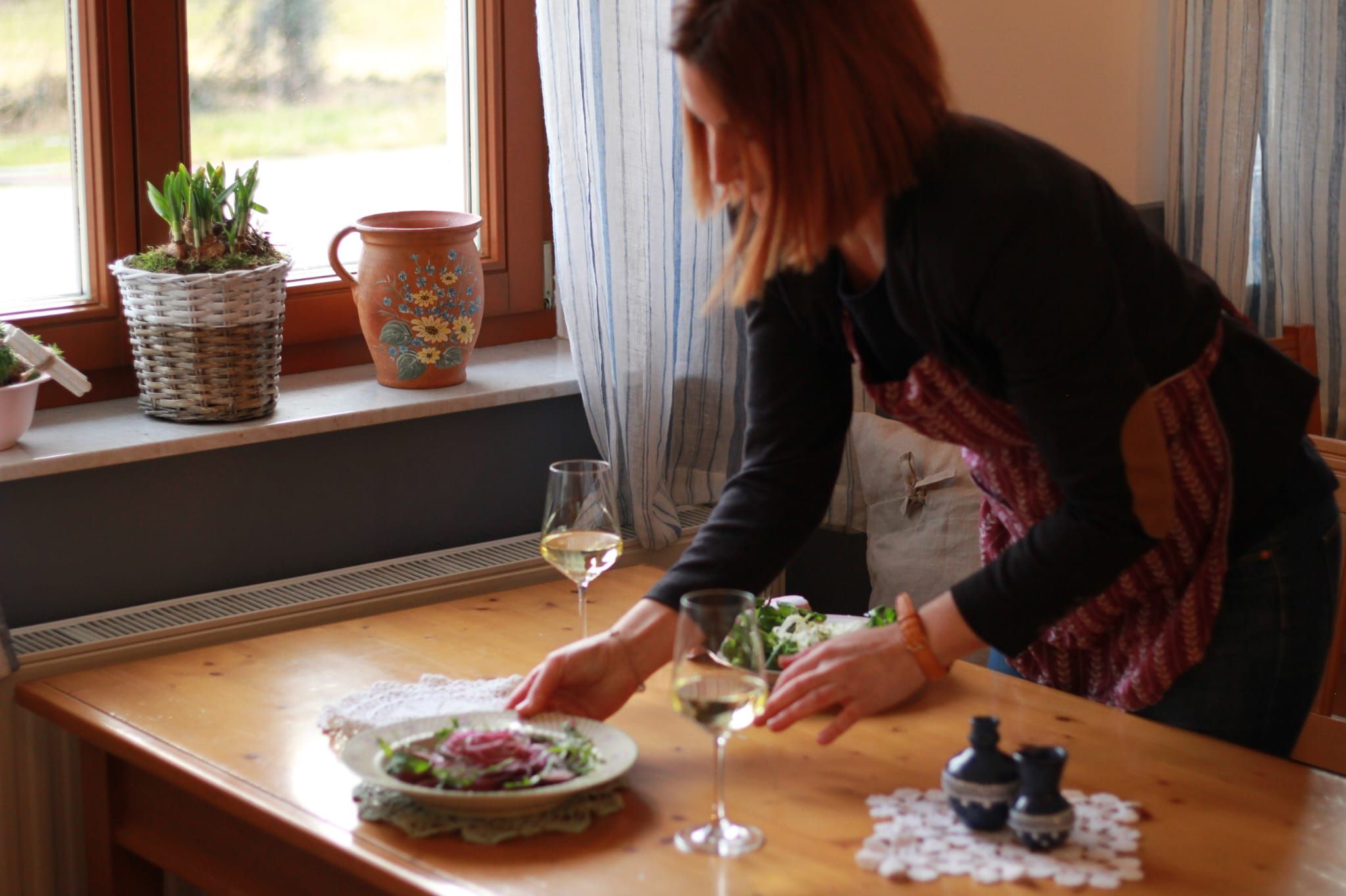 A woman sets a table with salad and white wine.
