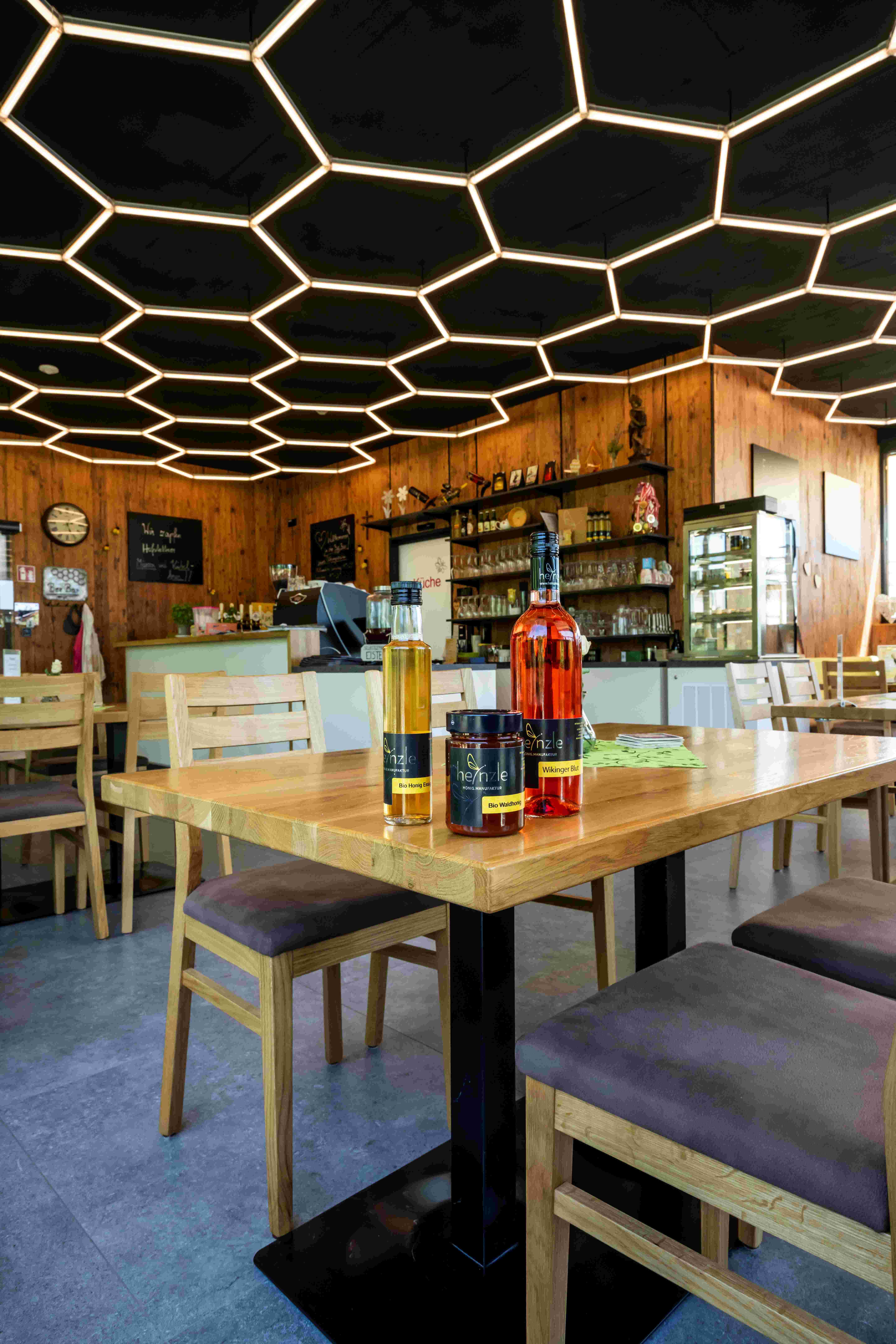 Interior view of a bar with honey-shaped ceiling lighting and honey products on a table.