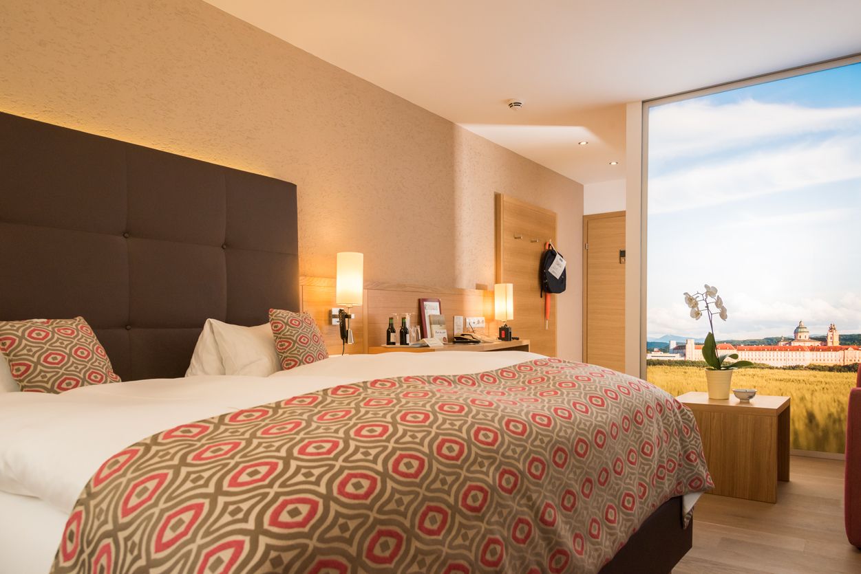 Modern hotel room with double bed, stylish lamps and large window with landscape view.