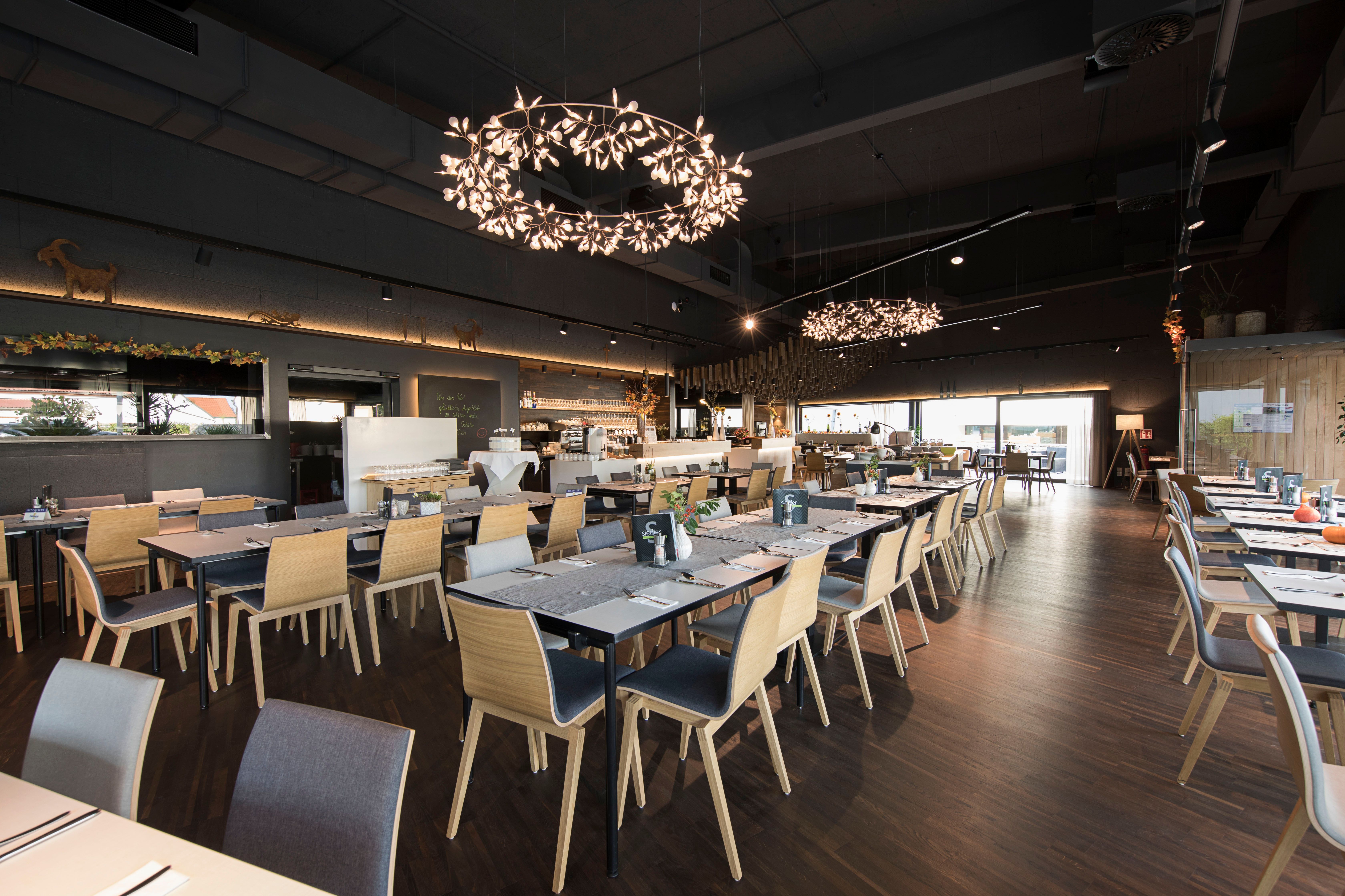 Modern restaurant with wooden chairs and decorative chandeliers.
