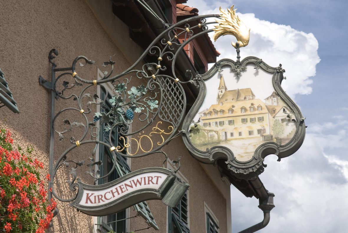 An artistically designed inn sign with the inscription 'Kirchenwirt' and a picture of a building with a church tower.