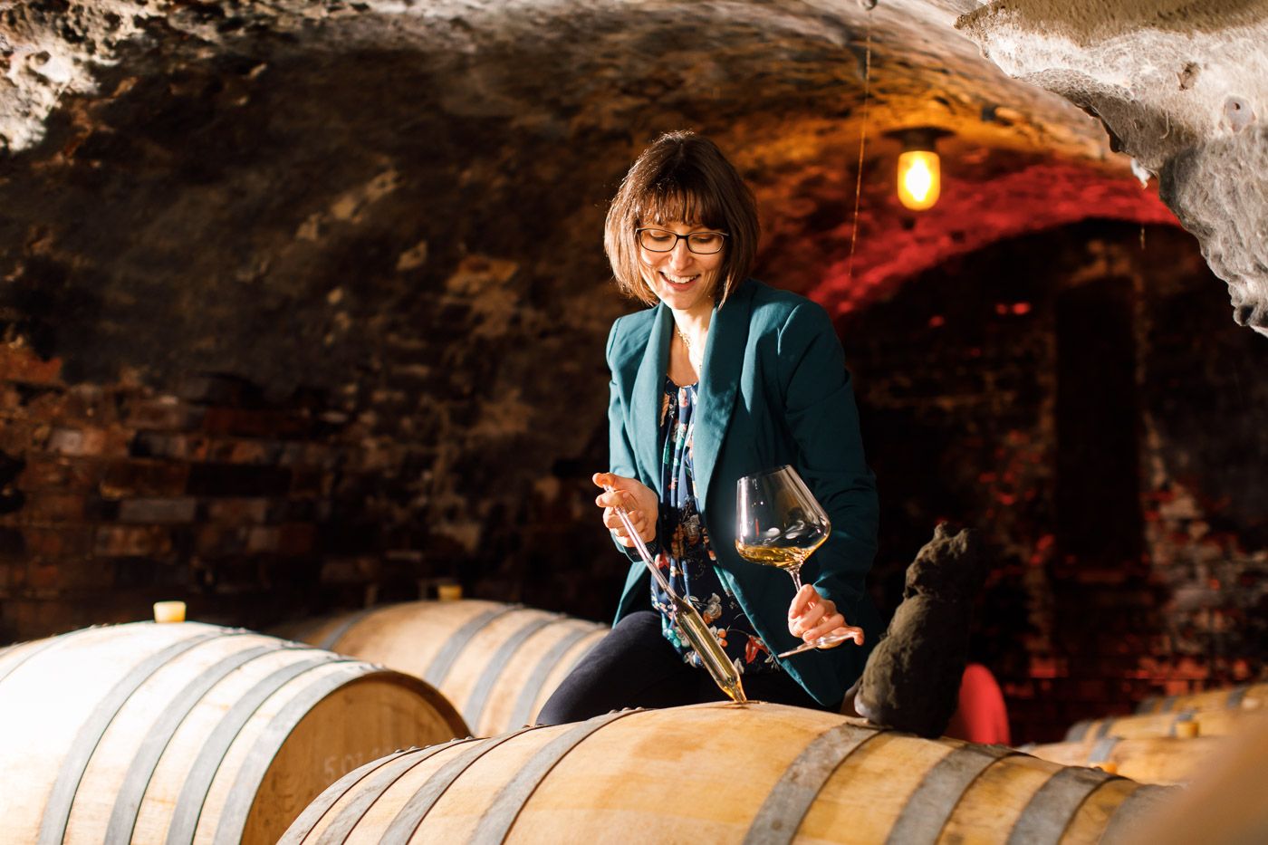 Woman tasting wine in the wine cellar with wine glass and barrel.