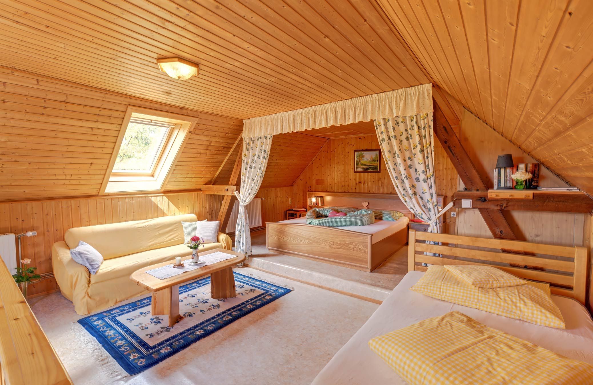 Cozy bedroom with wooden walls, a bed, sofa and skylight.