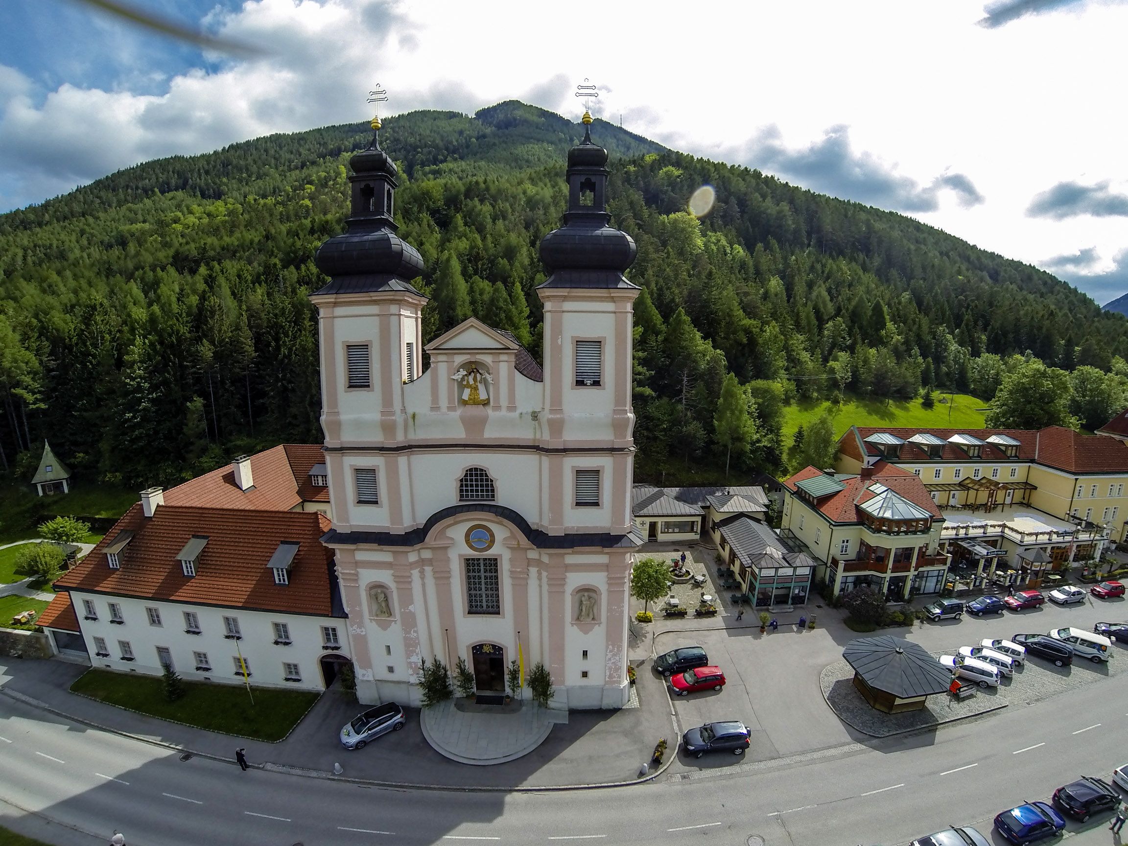 Aerial view of a church with two towers, surrounded by buildings and forest.