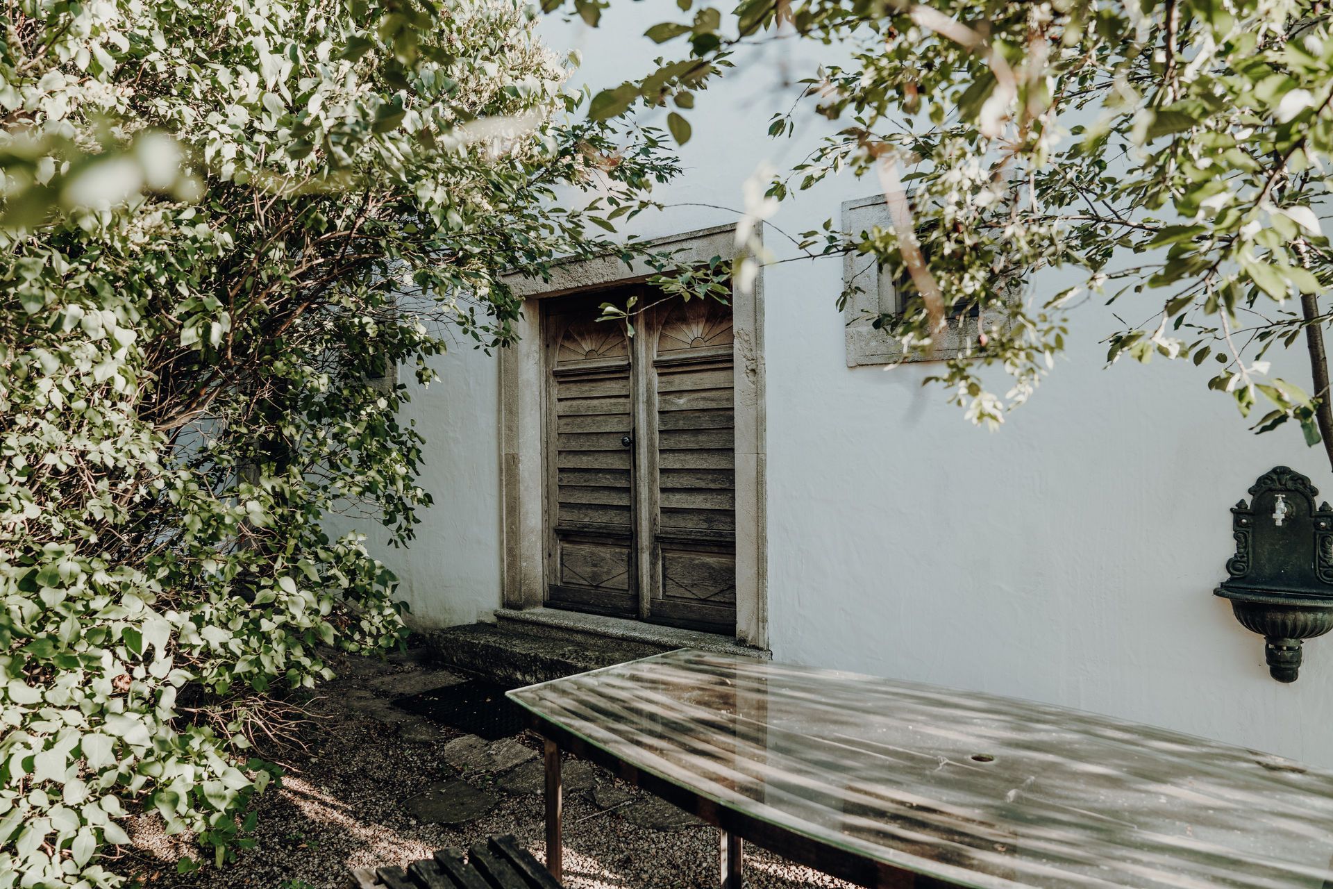 Wooden door behind trees with table in the foreground.