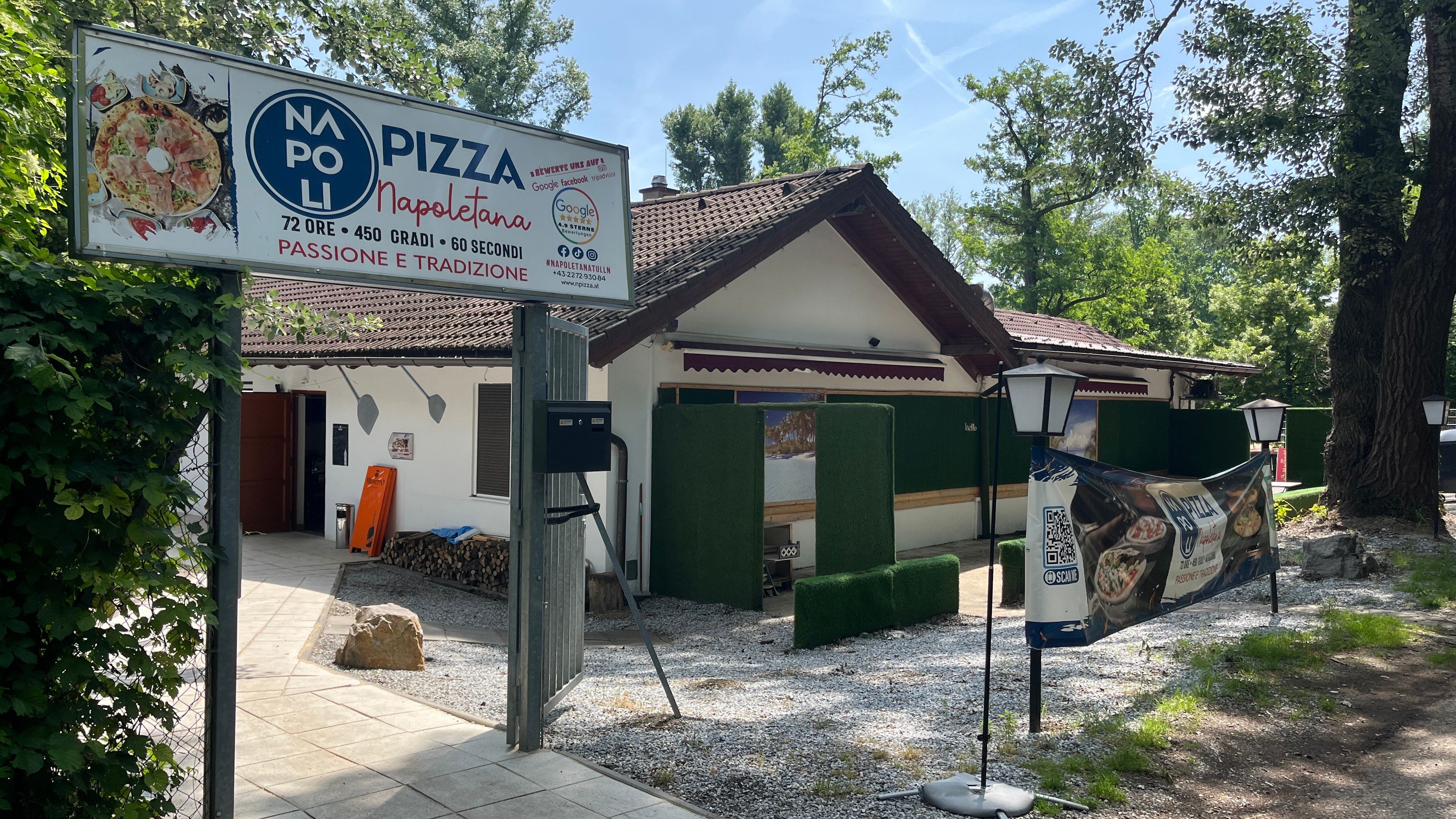 Entrance area as seen from the parking lot. Entrance gate with large pizzeria sign and lanterns.