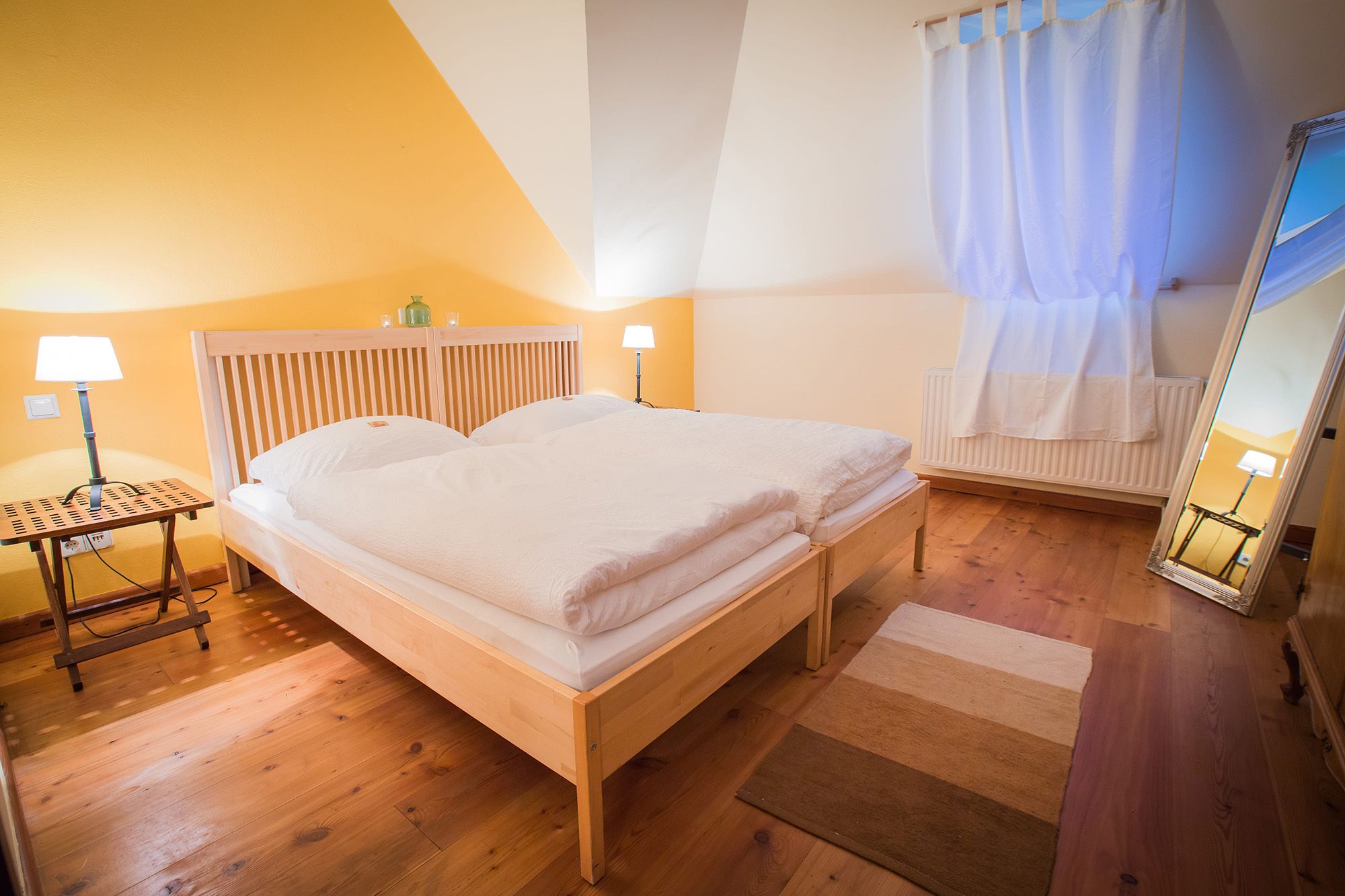 Cozy bedroom with double bed, wooden floor, yellow wall and large mirror.