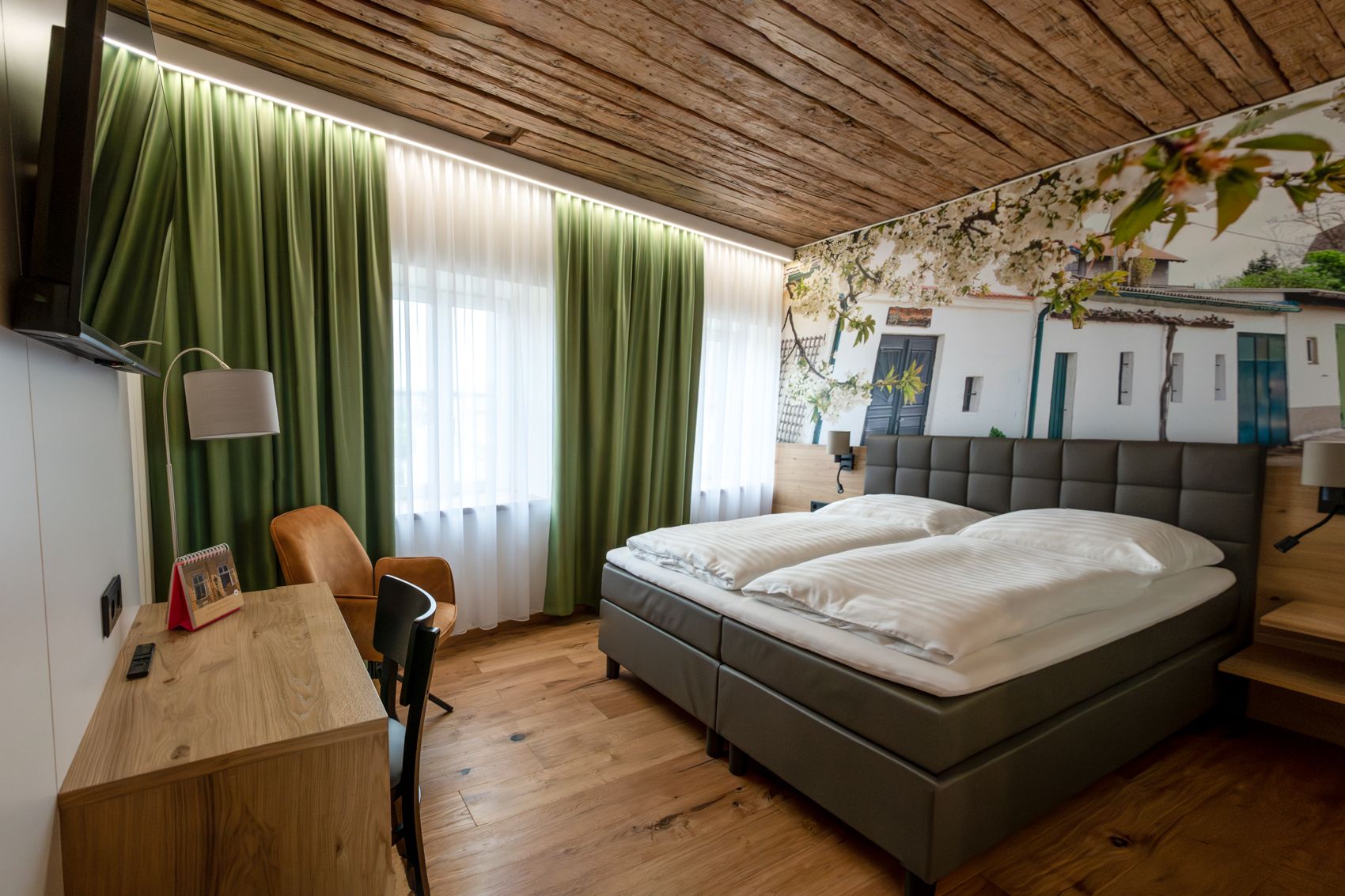 Modern guest room with double bed, wooden floor and green curtains.
