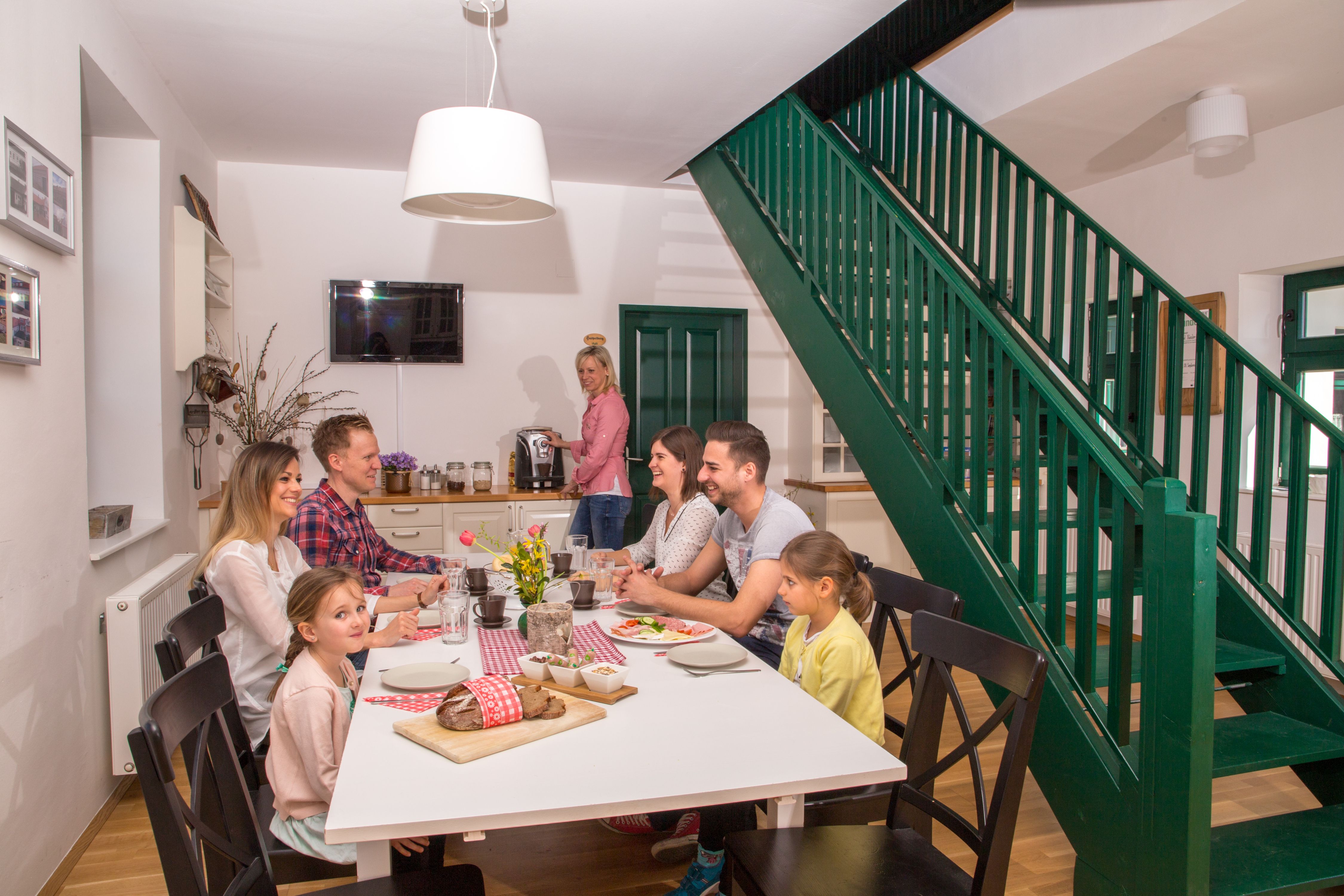 A family sits at a dining table in a modern room with a green staircase.