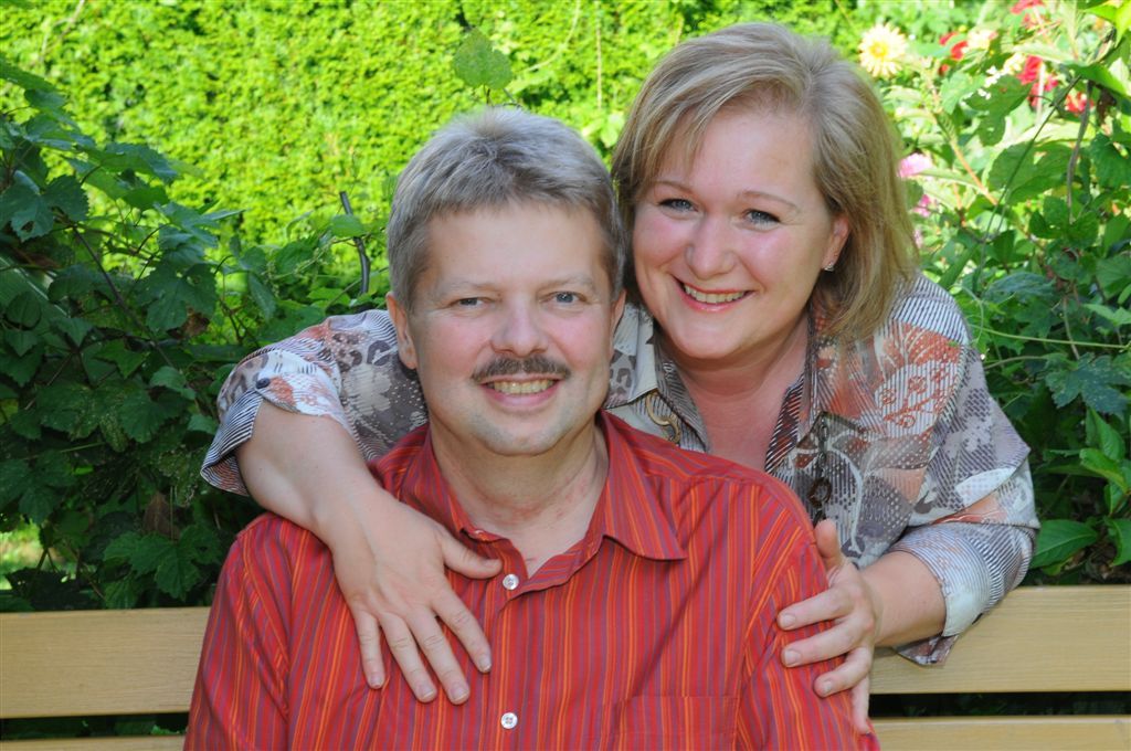 A smiling couple sits on a bench in the garden.