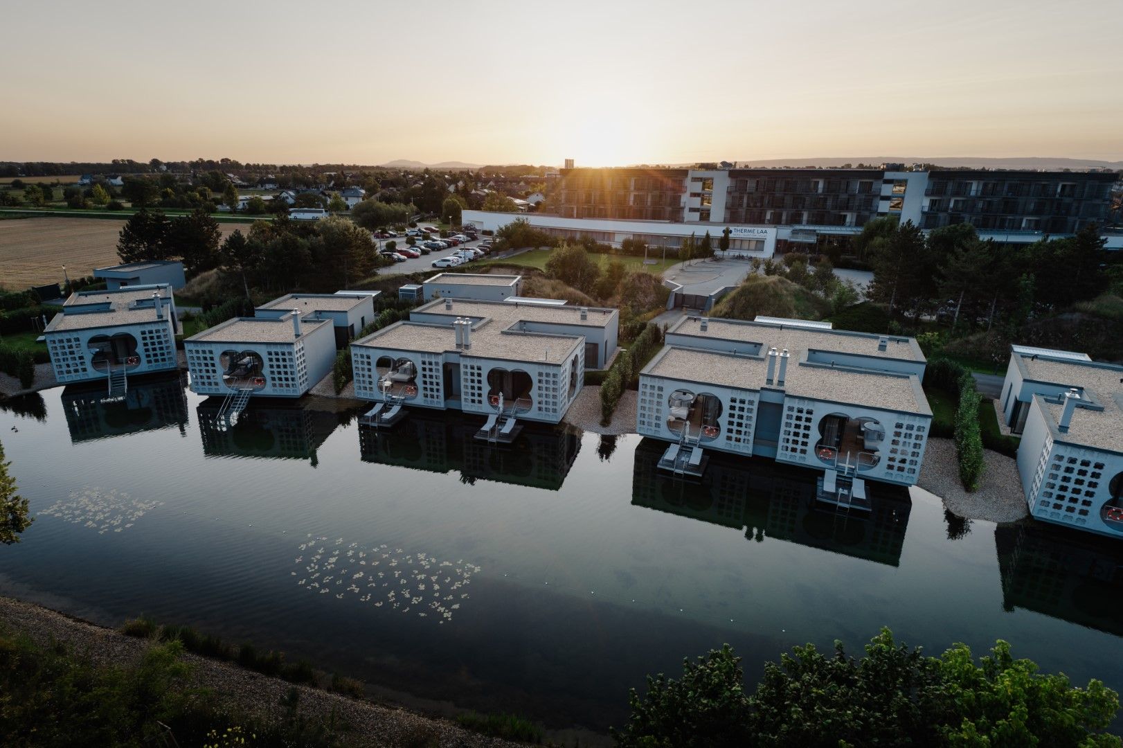 Aerial view of modern buildings on the waterfront at the Laa thermal spa resort at sunset.