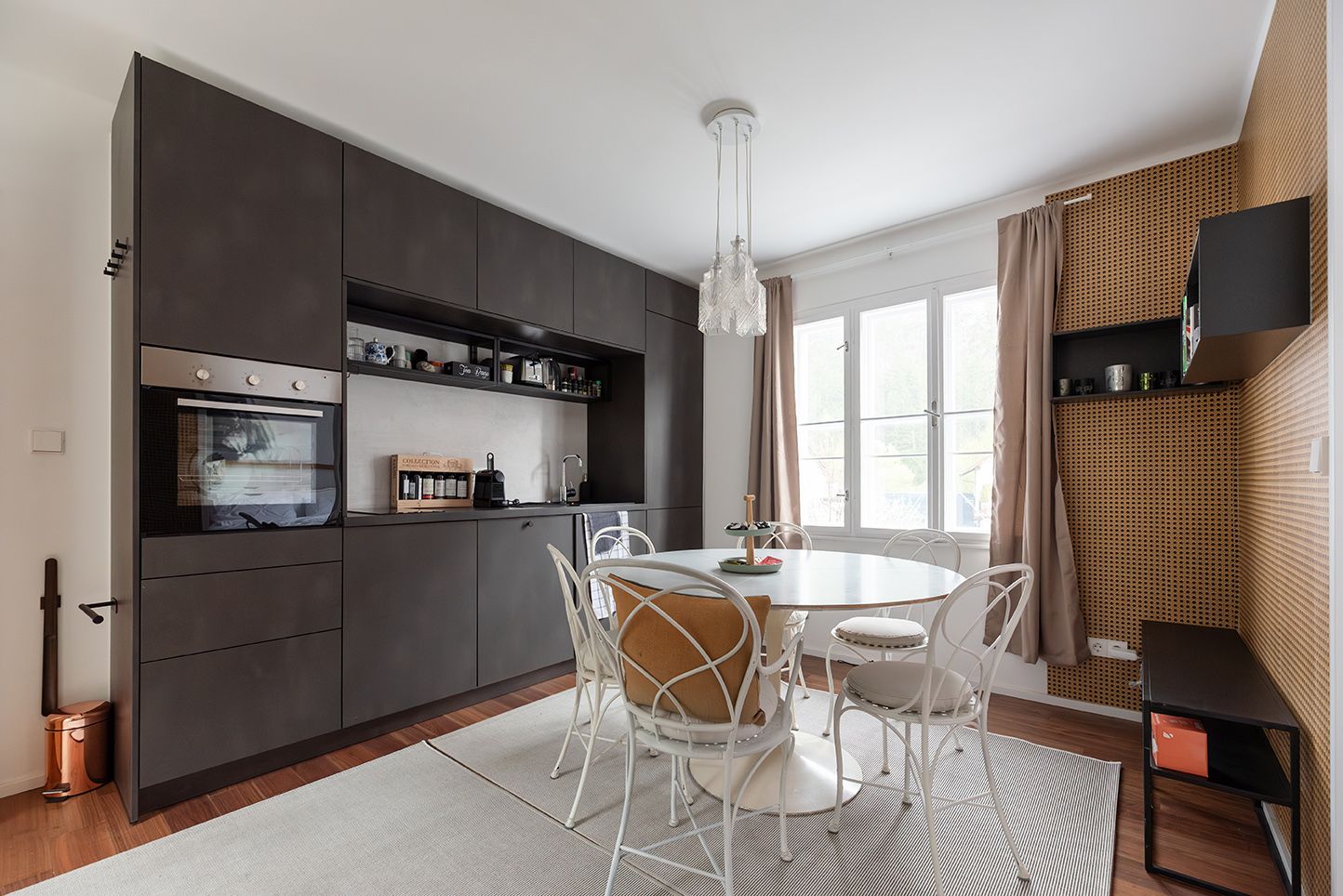 Modern kitchen with dark cupboards, dining table and chairs in front of a window.